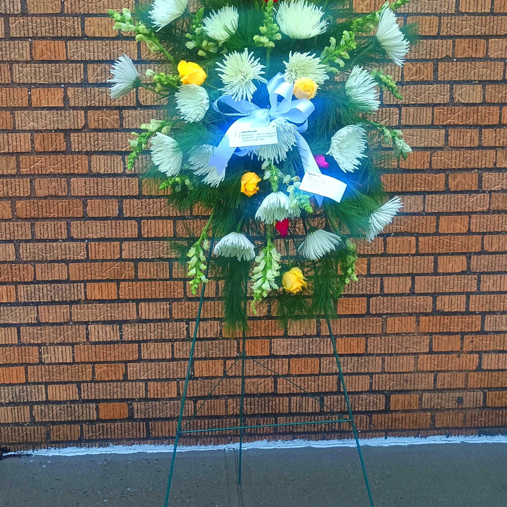 Standing floral spray with white and yellow blooms on a blue ribboned easel