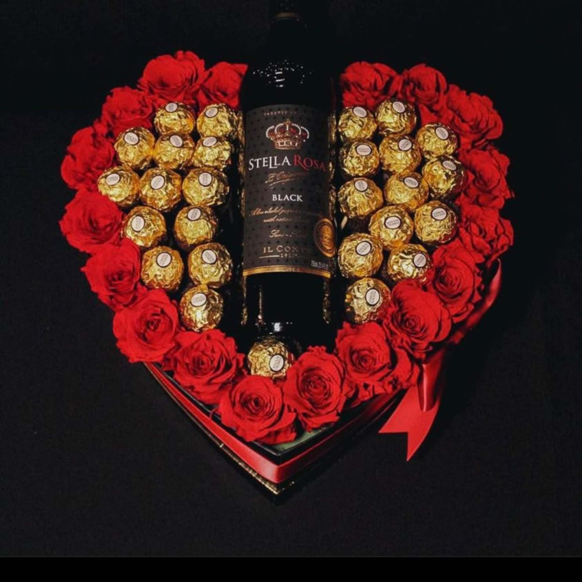 Heart-shaped gift box with red roses, gold chocolates, and a wine bottle