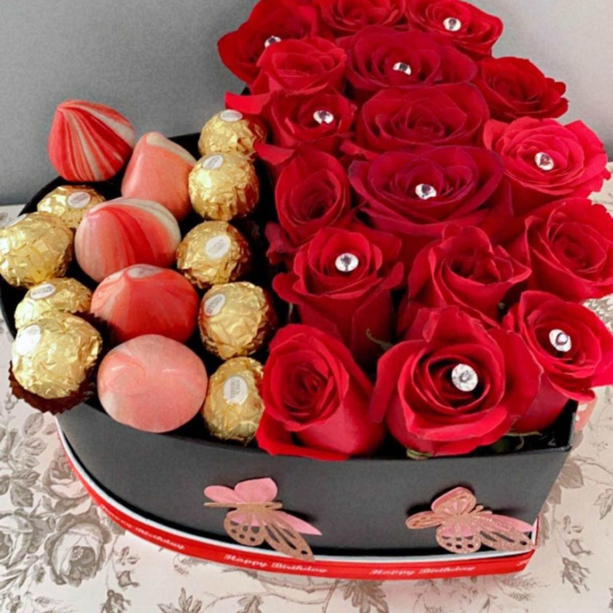Red roses arranged with assorted chocolates in a black heart-shaped box