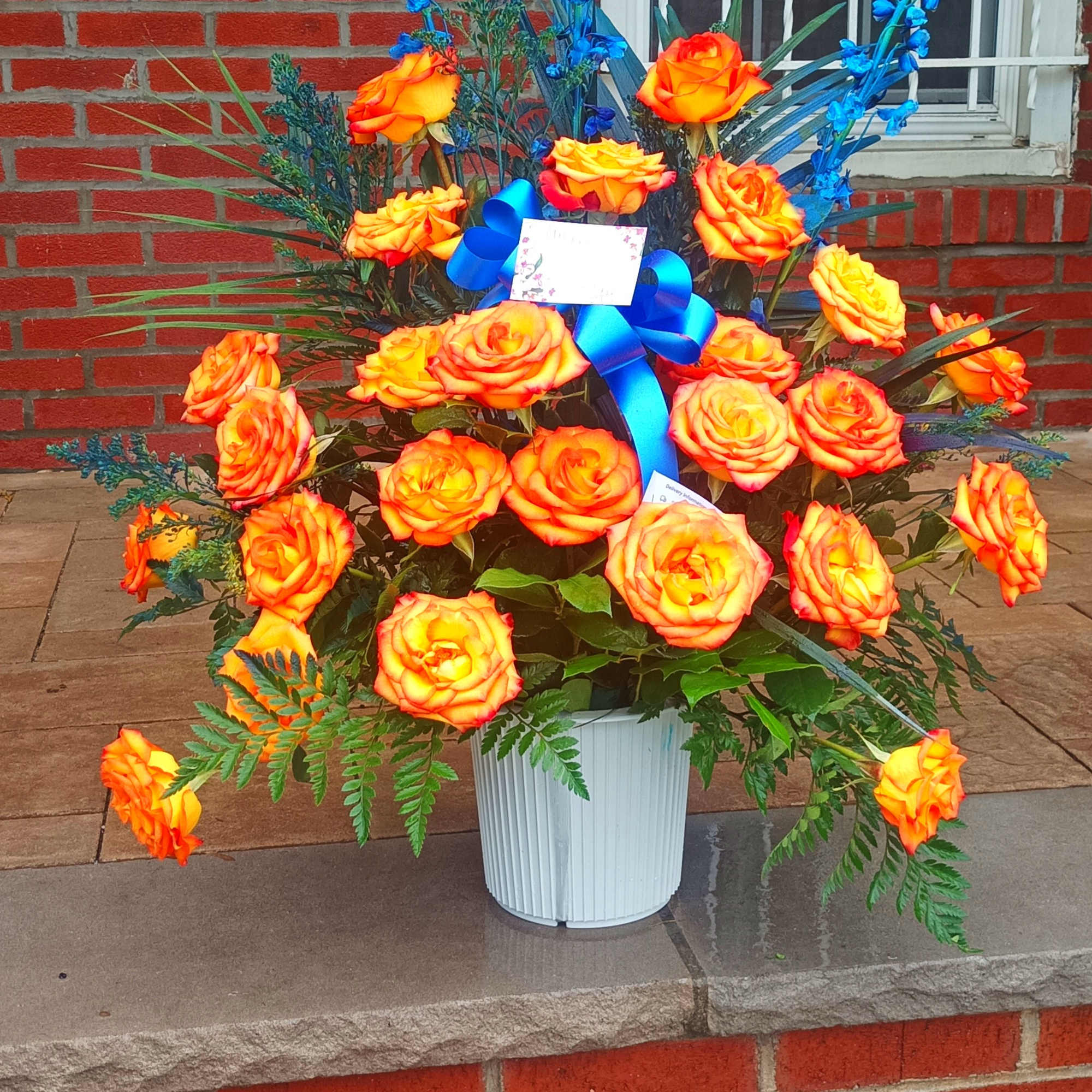Orange roses in a white container with blue accents.