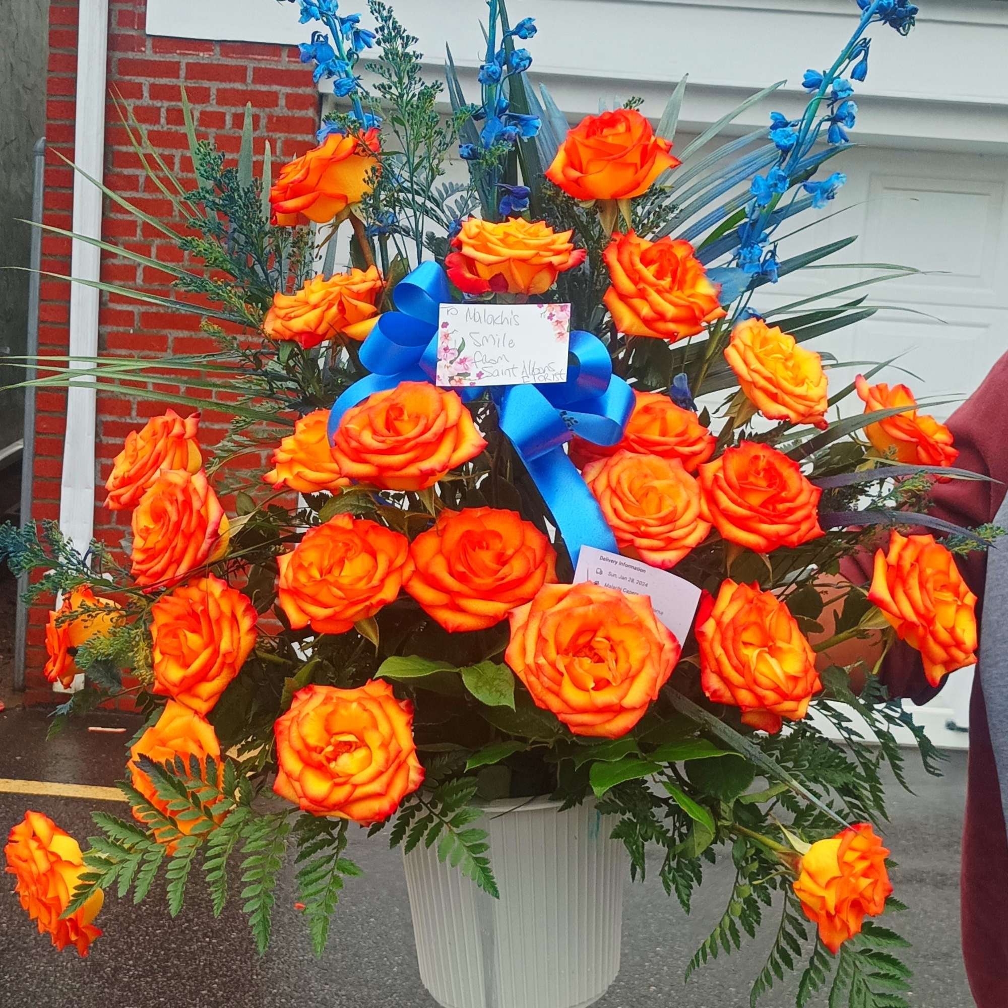 Large orange rose arrangement in a white container with blue ribbon