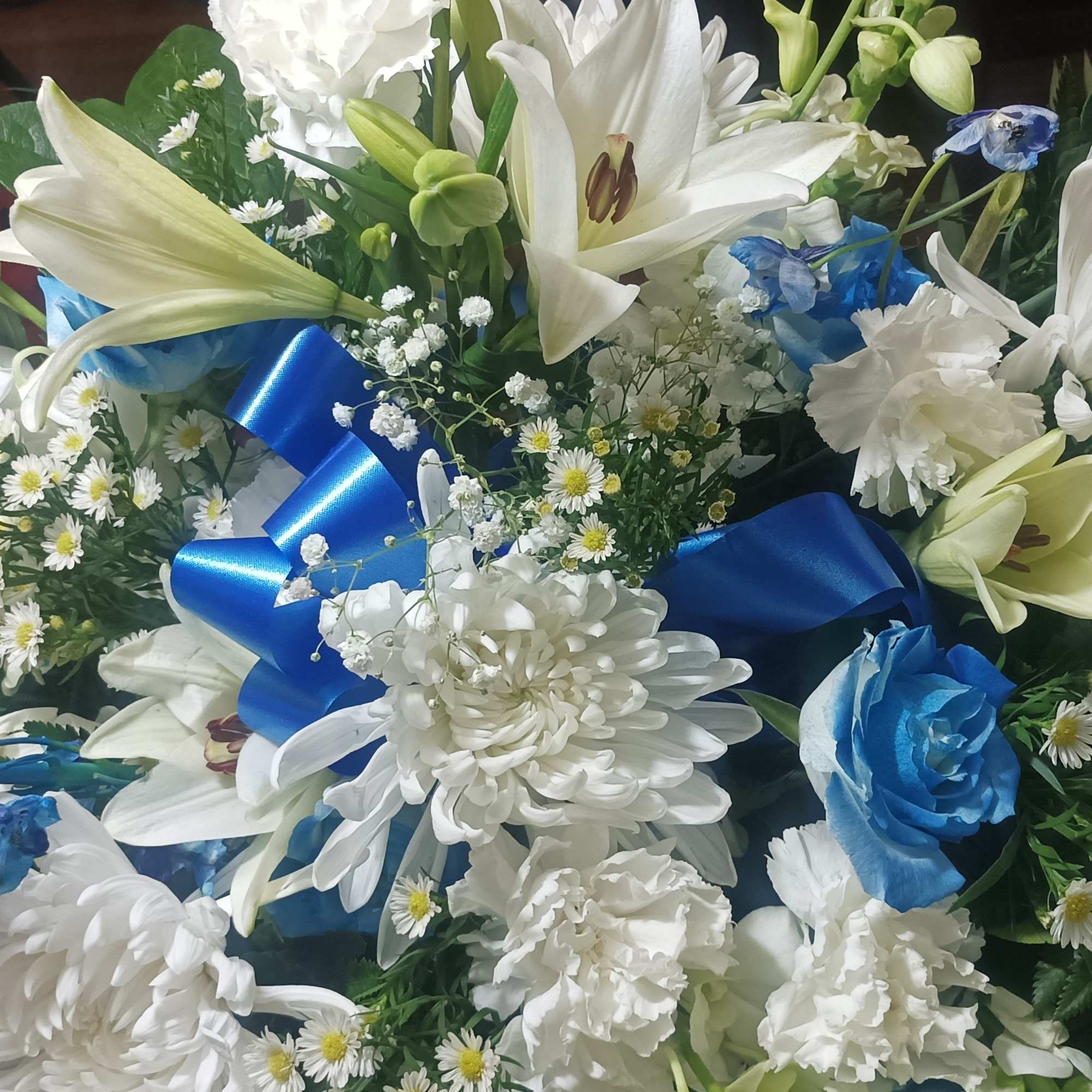 Blue and white floral arrangement with lilies, daisies, and ribbon