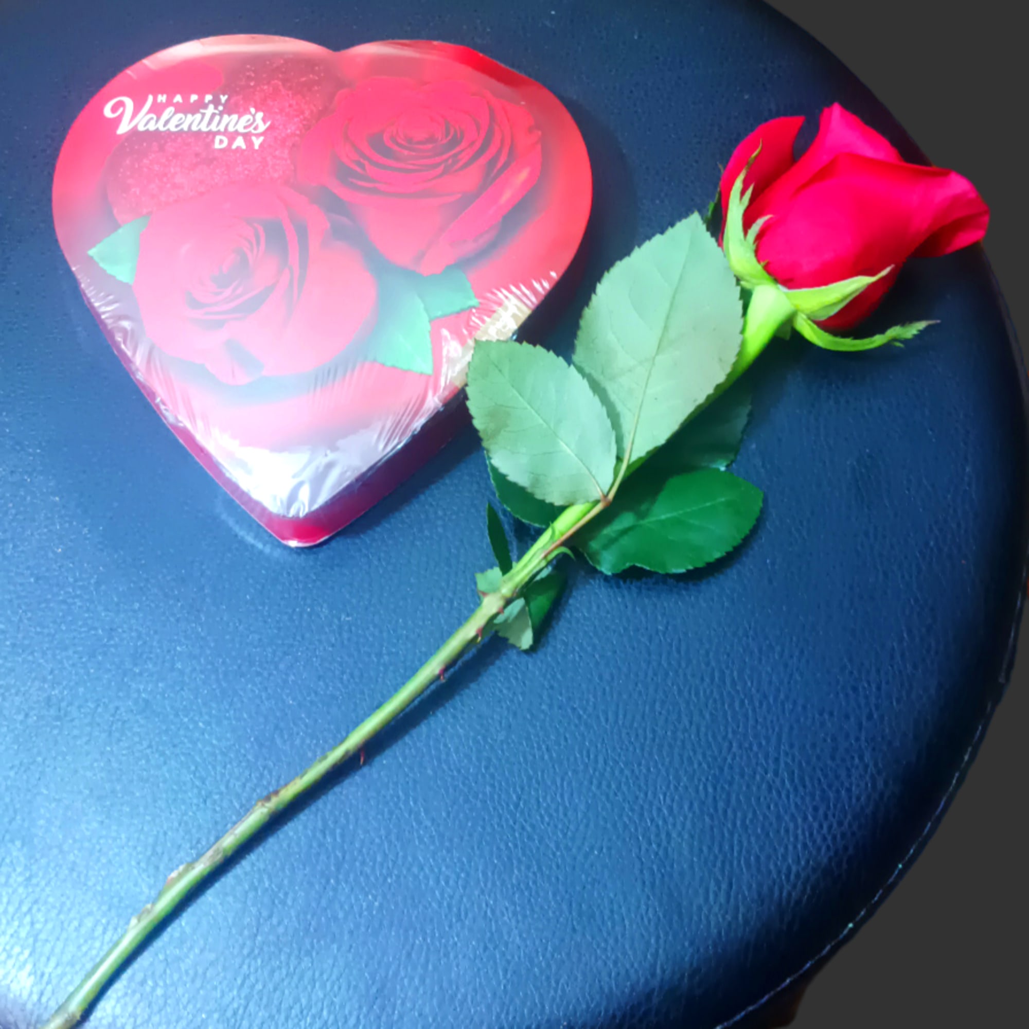 Single red rose beside a heart-shaped Valentine candy box