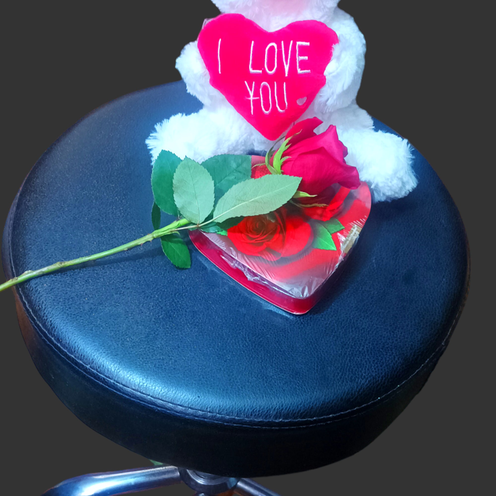 White teddy bear holding a pink heart with a red rose on a stool