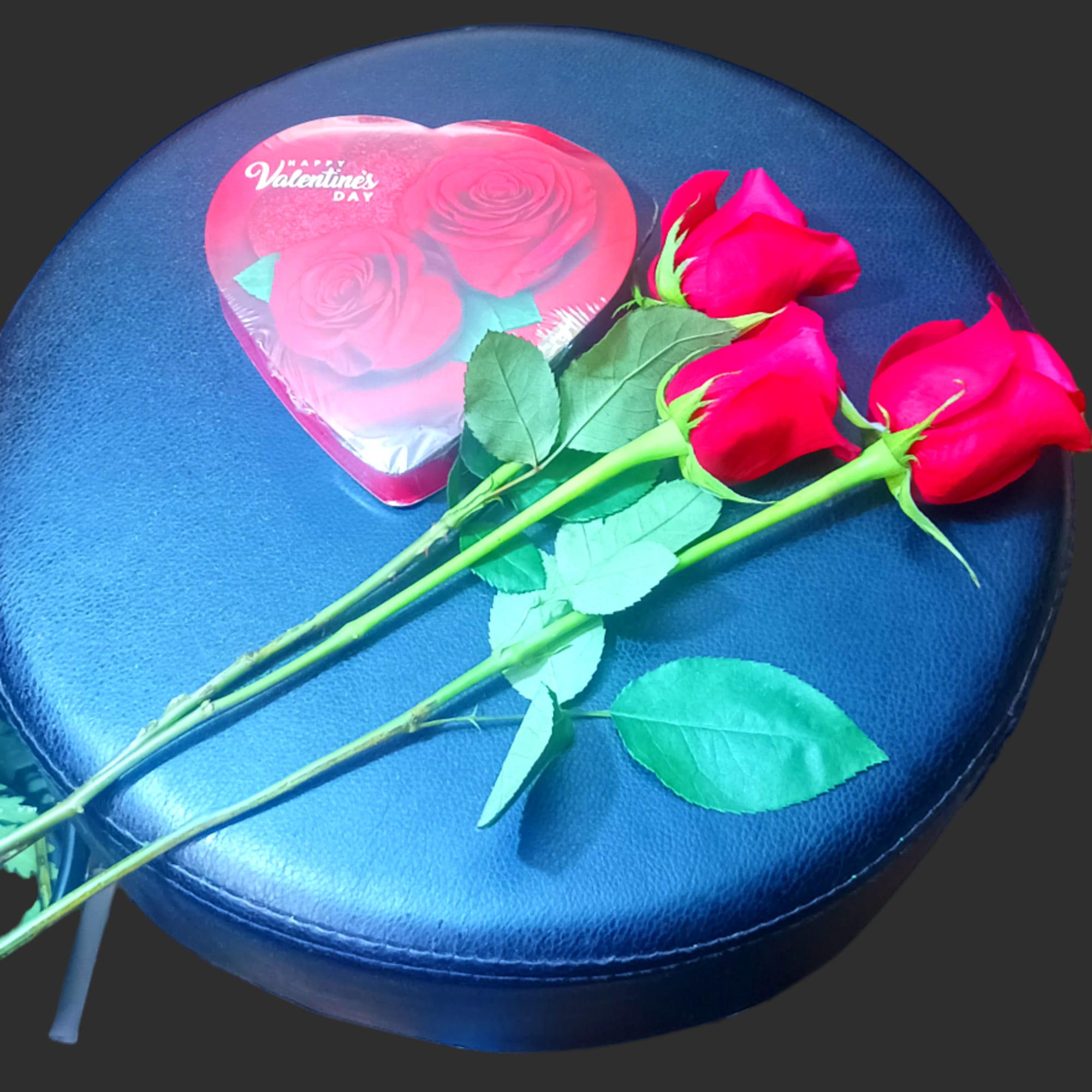 Three red roses with a heart-shaped Valentine card on a blue seat
