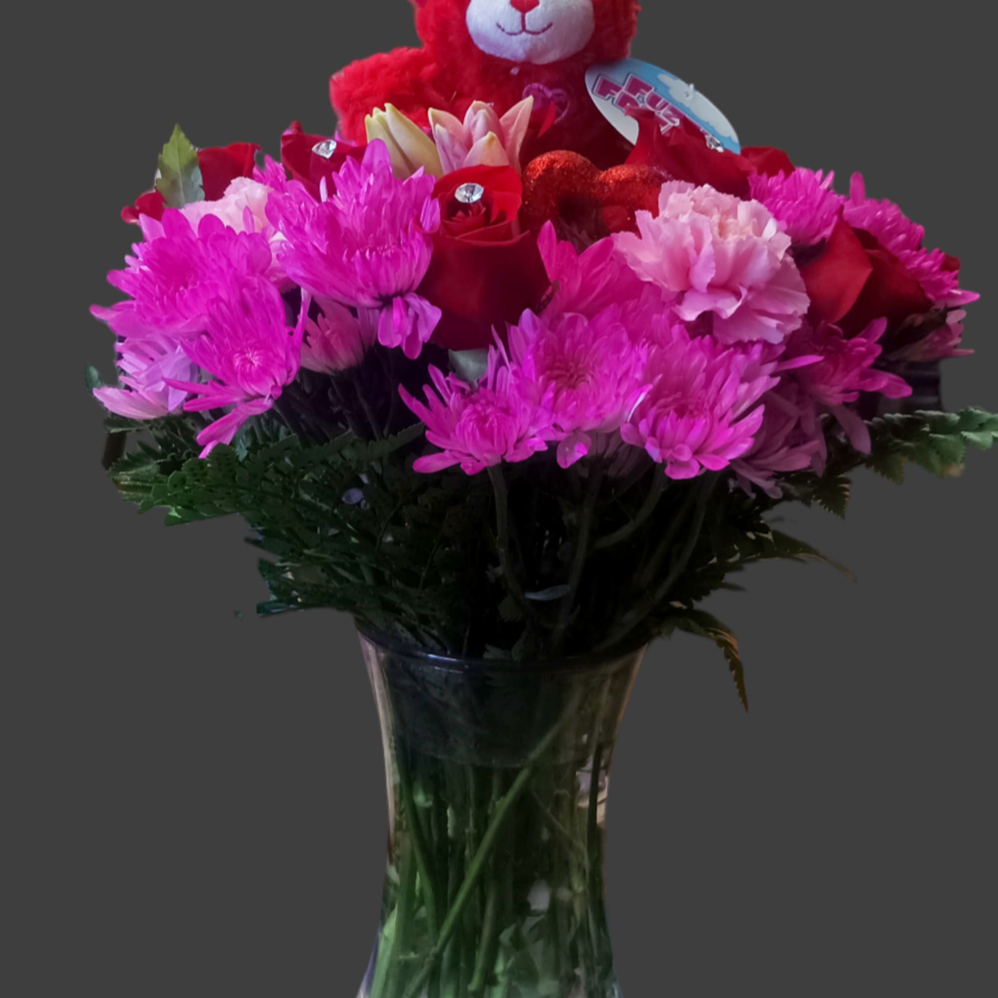 Bouquet of pink and red flowers in a glass vase with a red teddy bear