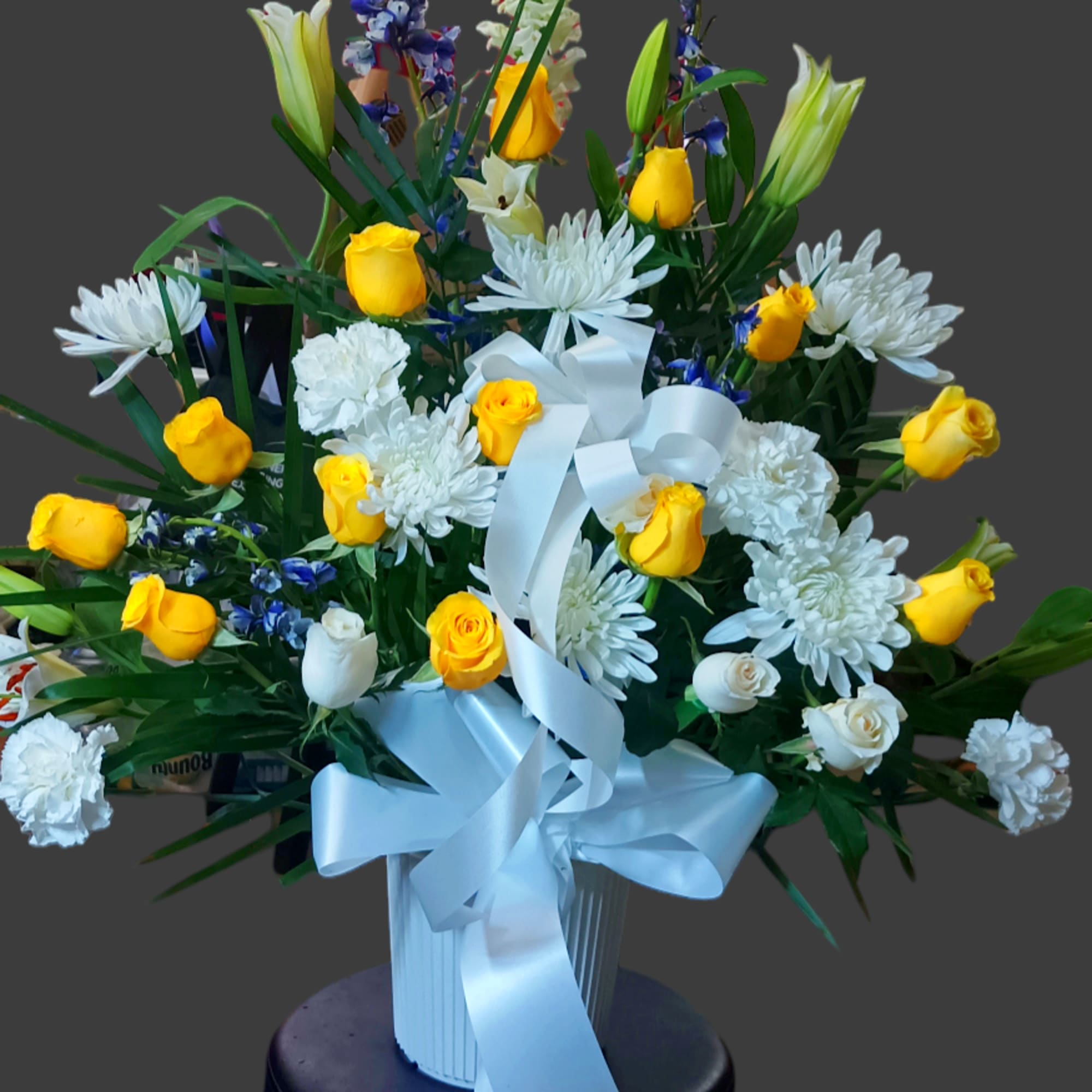 Bouquet of yellow and white flowers in a white vase with a blue ribbon