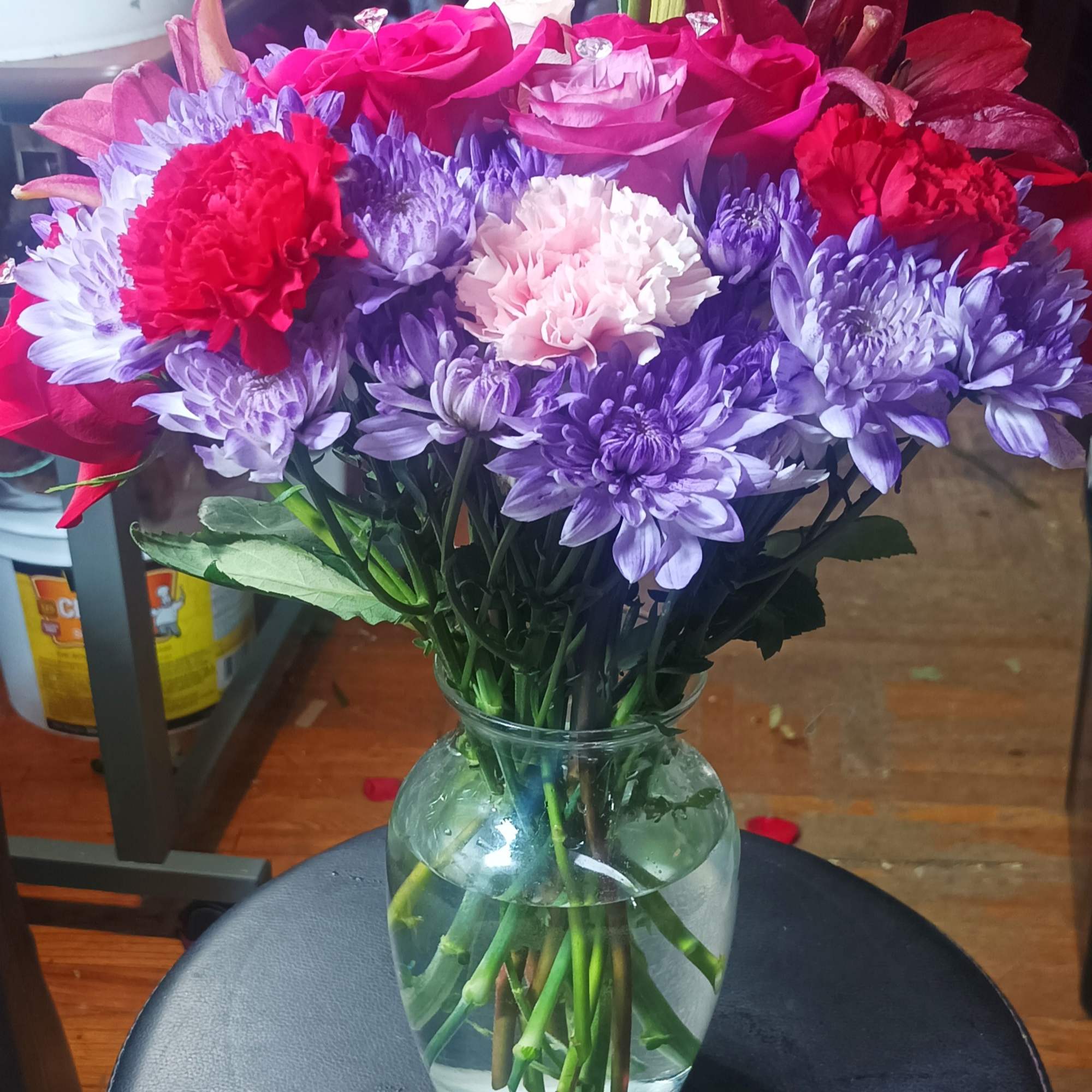 Mixed bouquet of pink roses, purple chrysanthemums, and red carnations in a glass vase