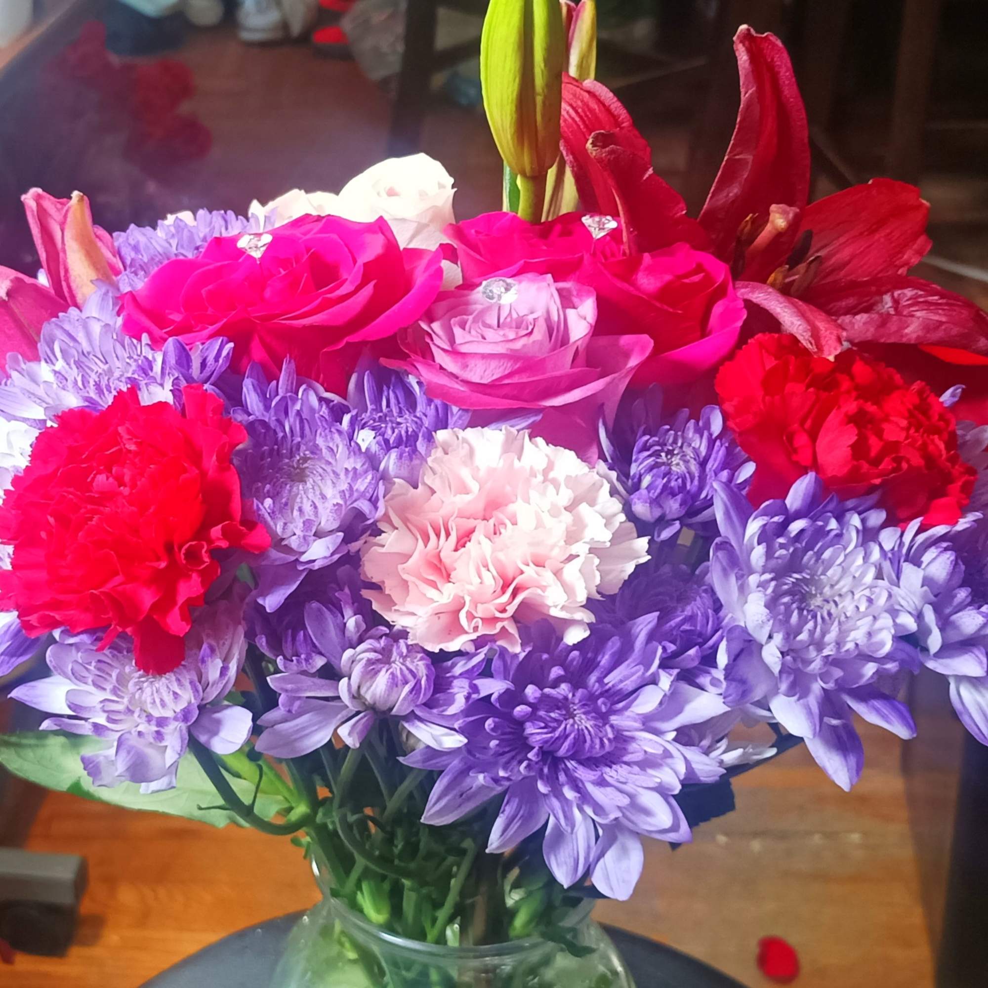 Bouquet of pink roses, purple chrysanthemums, and red carnations in a glass vase