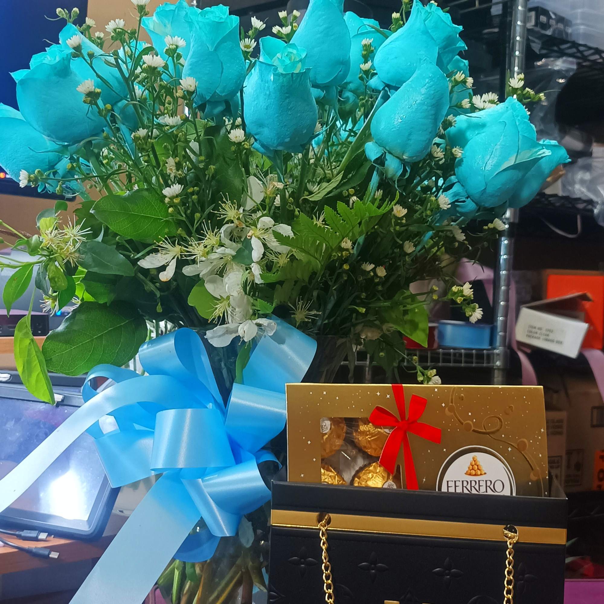 Blue roses in a glass vase with a ribbon and chocolates in front