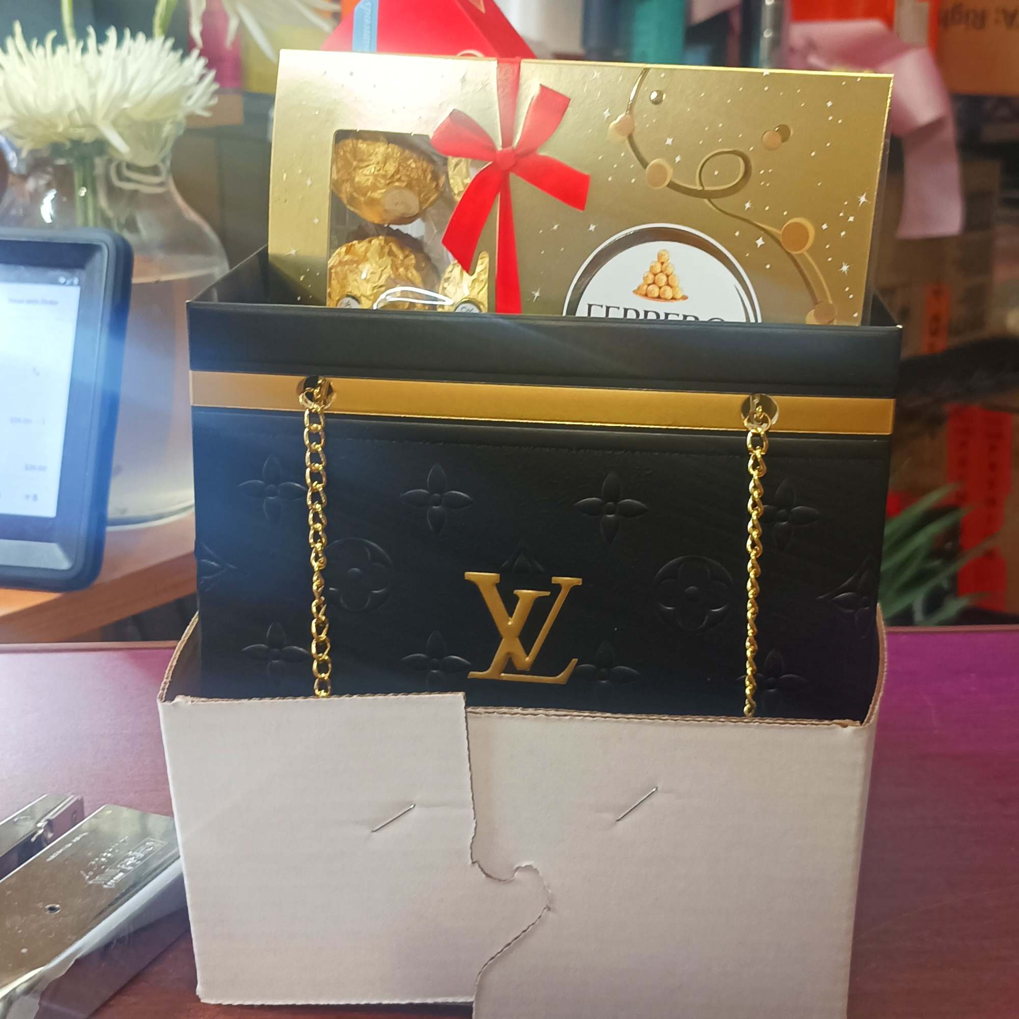 Gift bag with chocolates and a gold card, with white flowers in the background.