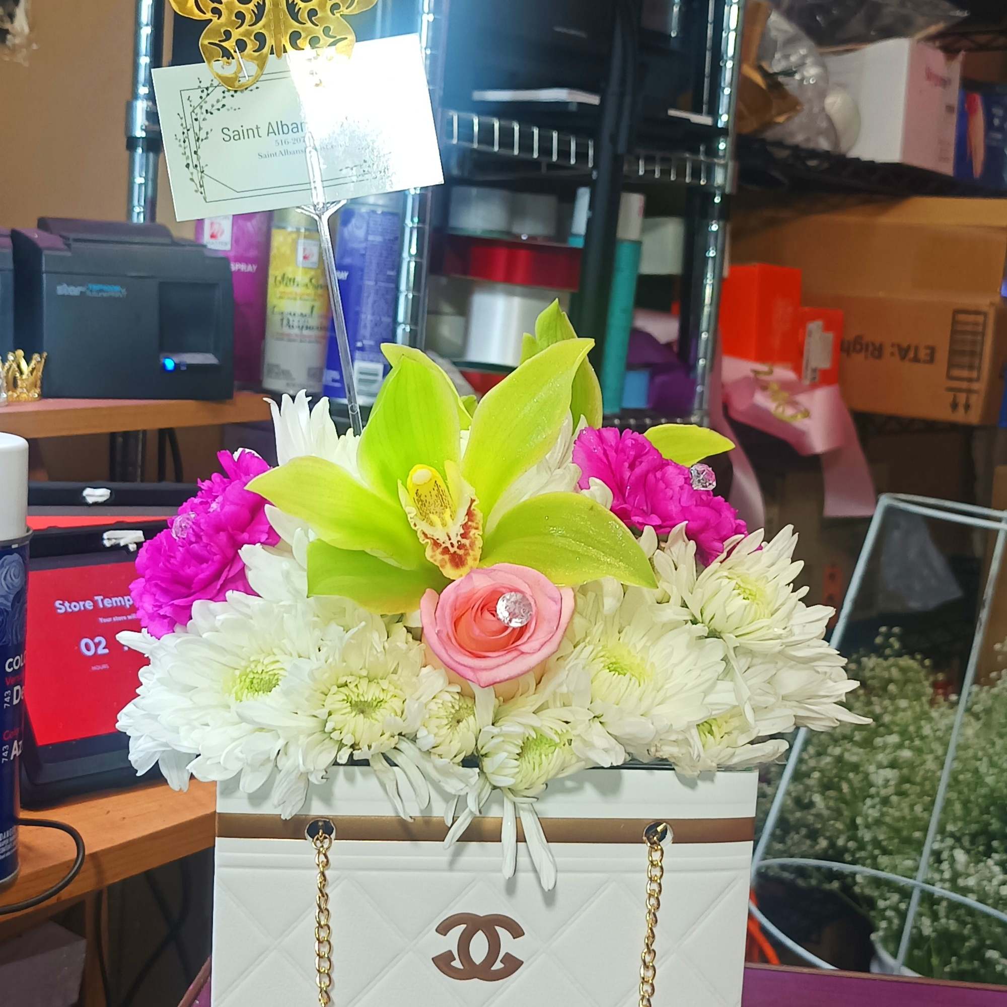 Flower arrangement in a white gift bag with a gold butterfly topper