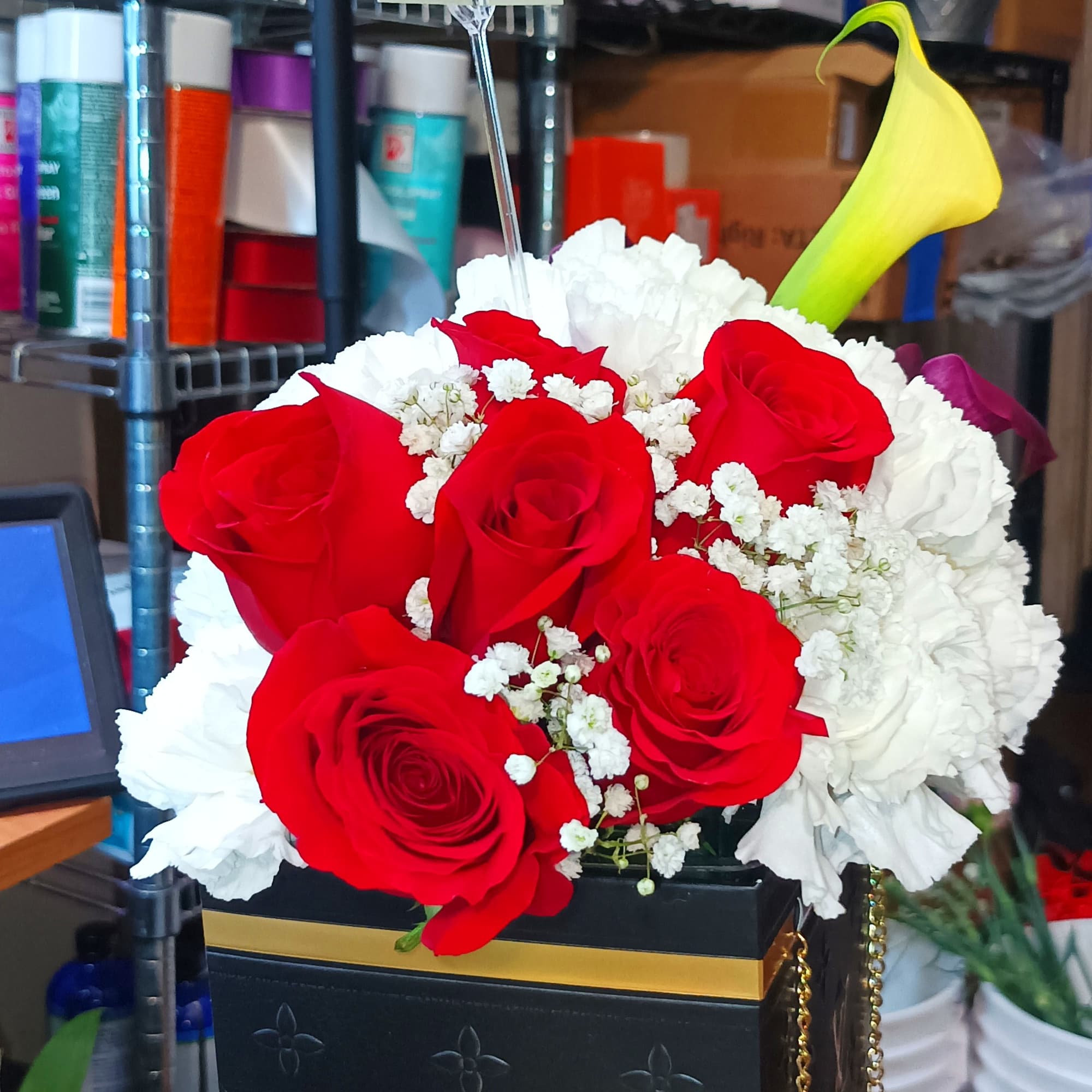 Red roses and white carnations in a black box with a yellow calla lily