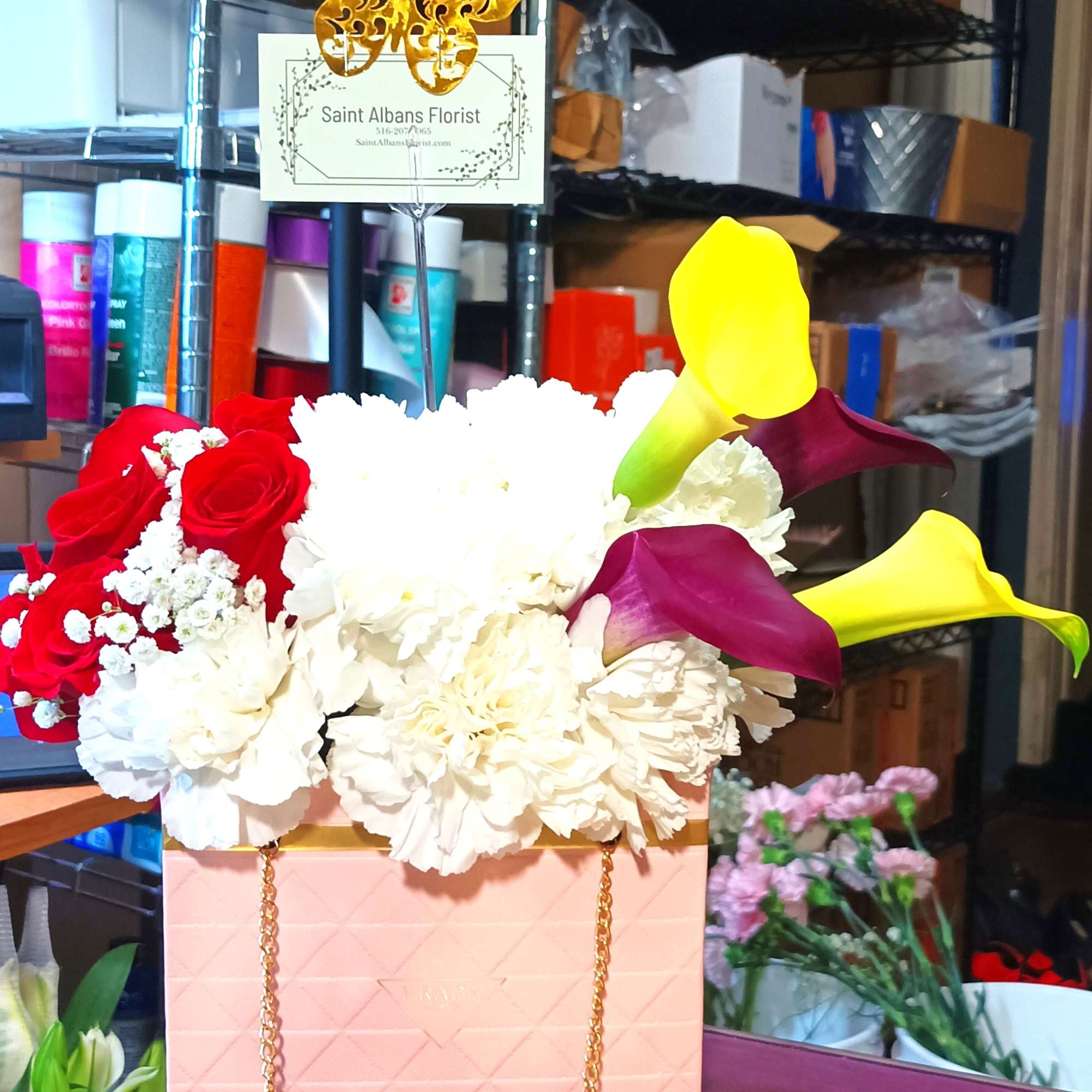 Flower gift arrangement with red roses, white blooms, calla lilies, and chocolates