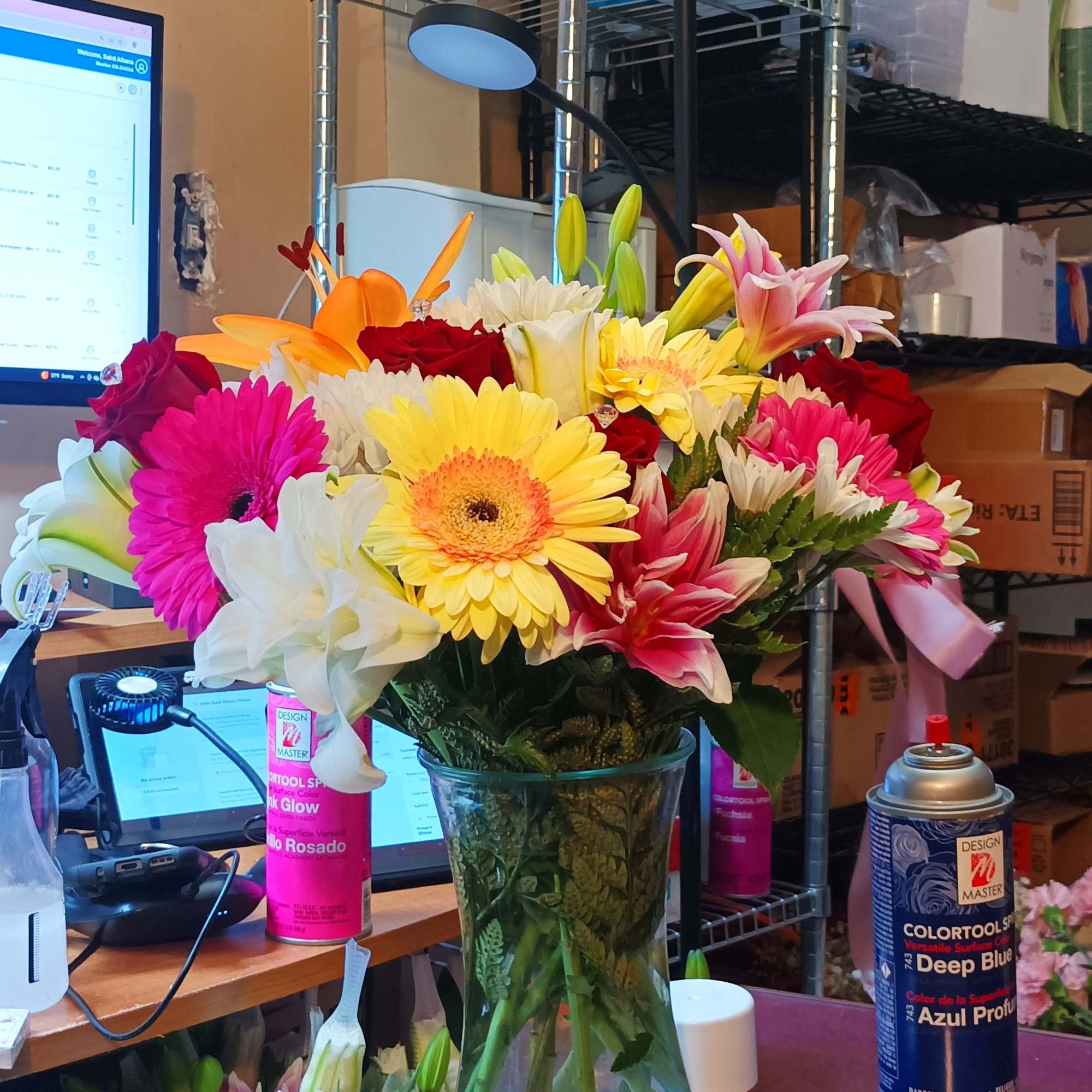 Mixed bouquet of bright gerbera daisies, lilies, and roses in a glass vase