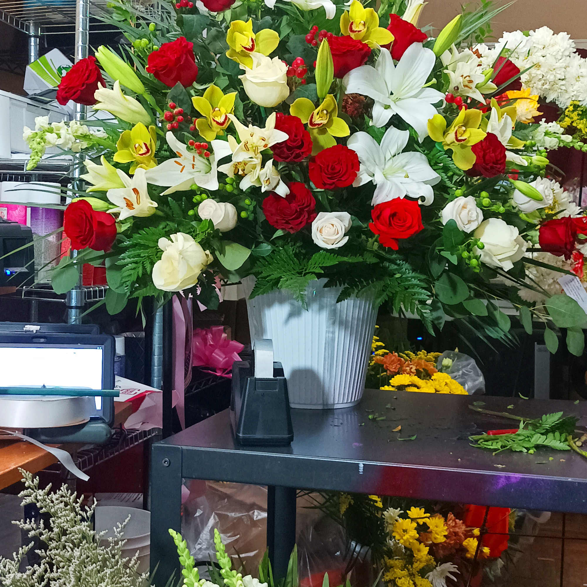 Large mixed flower arrangement in a white vase with red, white, and yellow blooms, photo 5 of 8