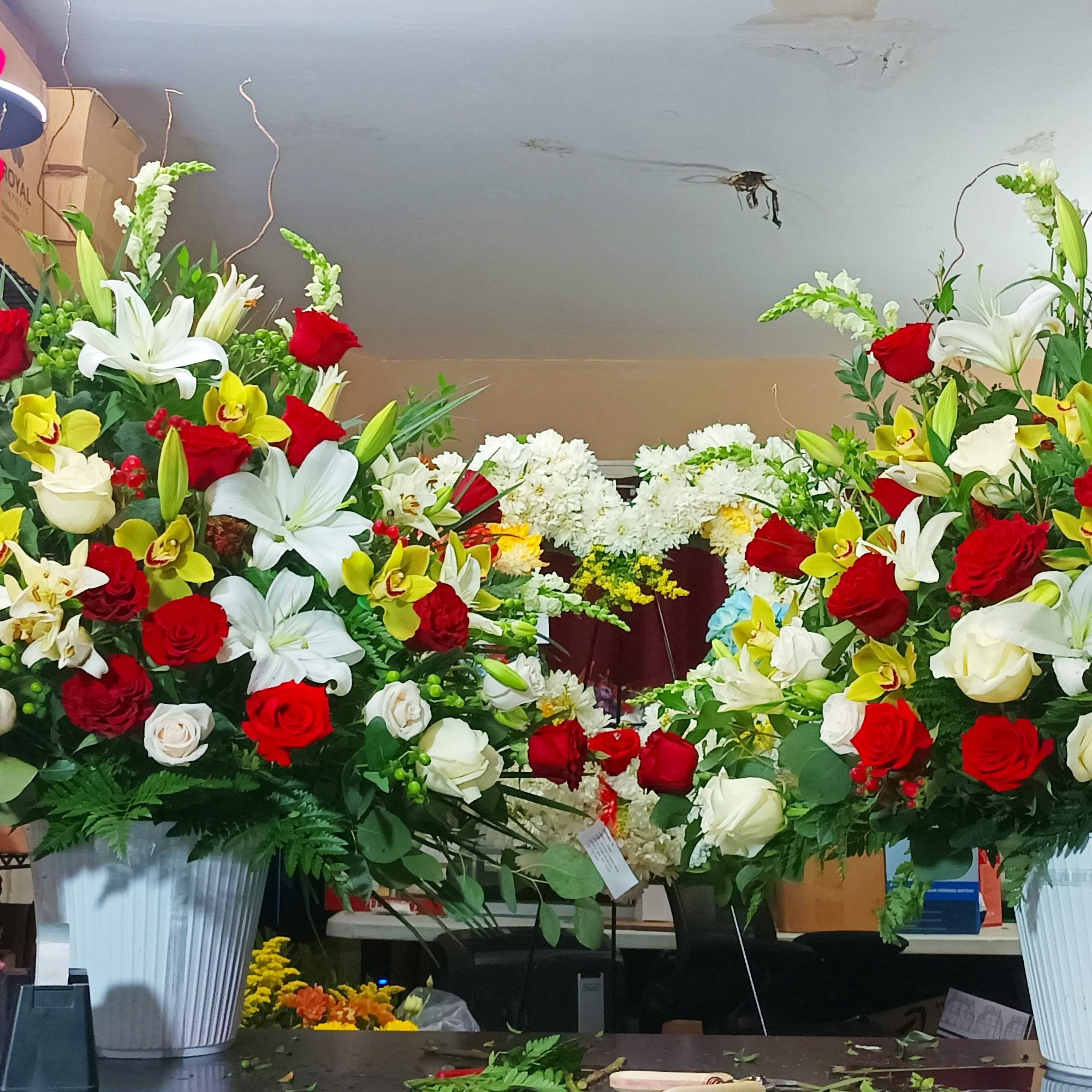 Two large floral arrangements with red, white, and yellow flowers in white containers.