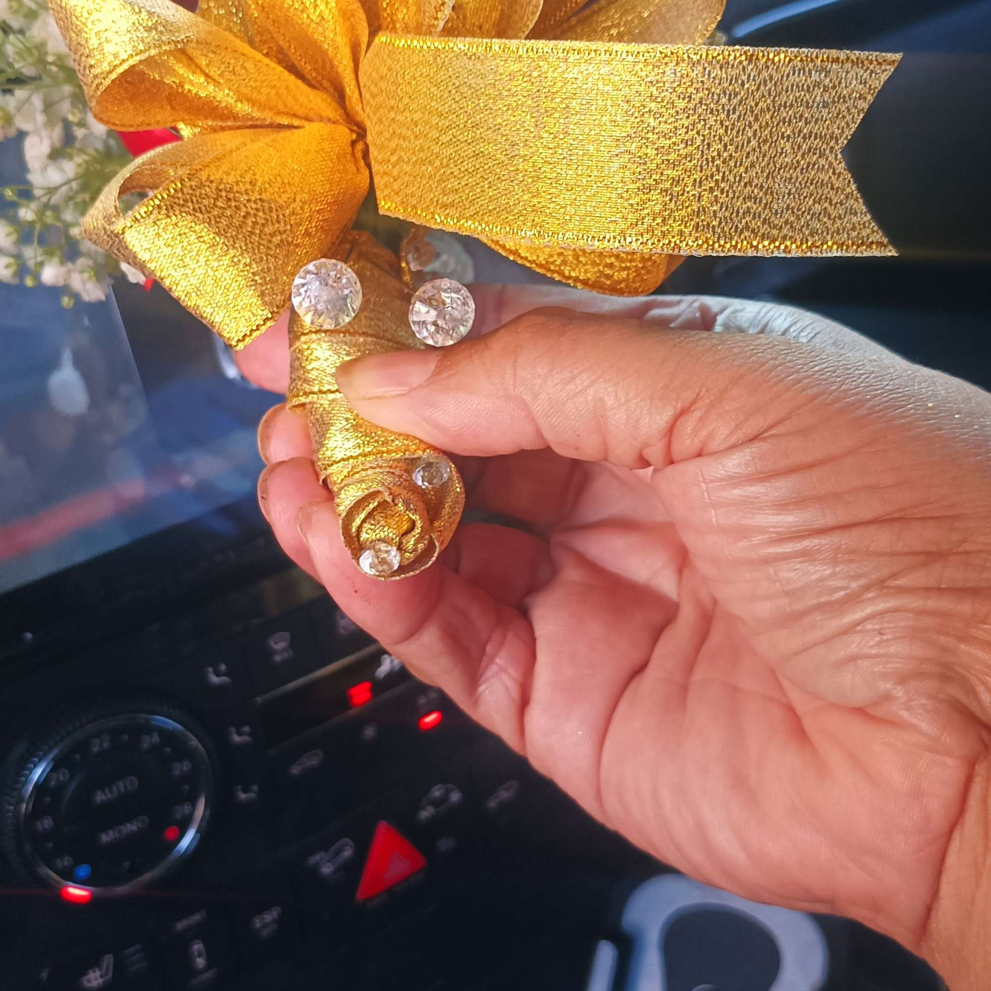 Hand holding a small red rose boutonniere with a gold ribbon bow