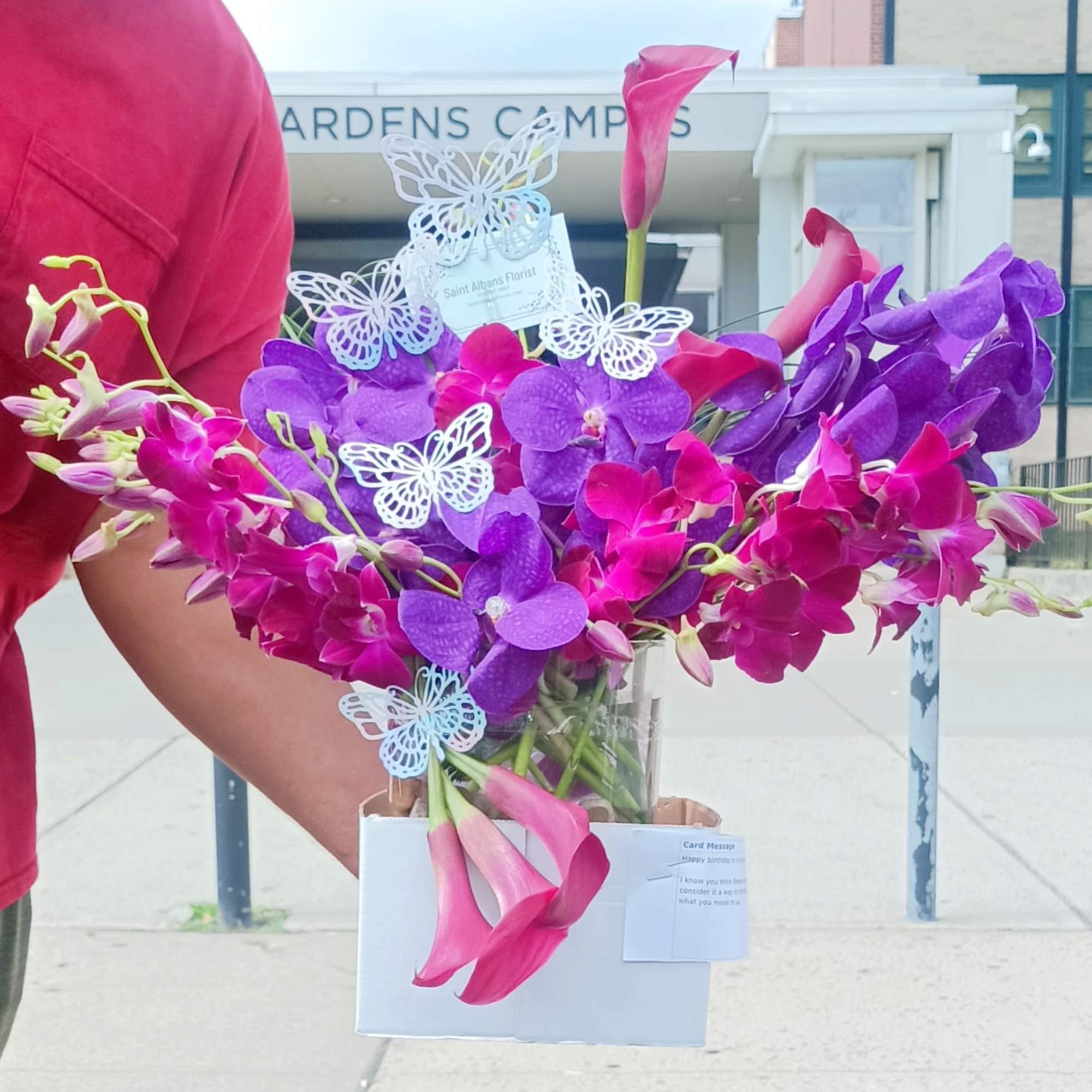 Pink and purple orchid arrangement in a white box with butterfly picks