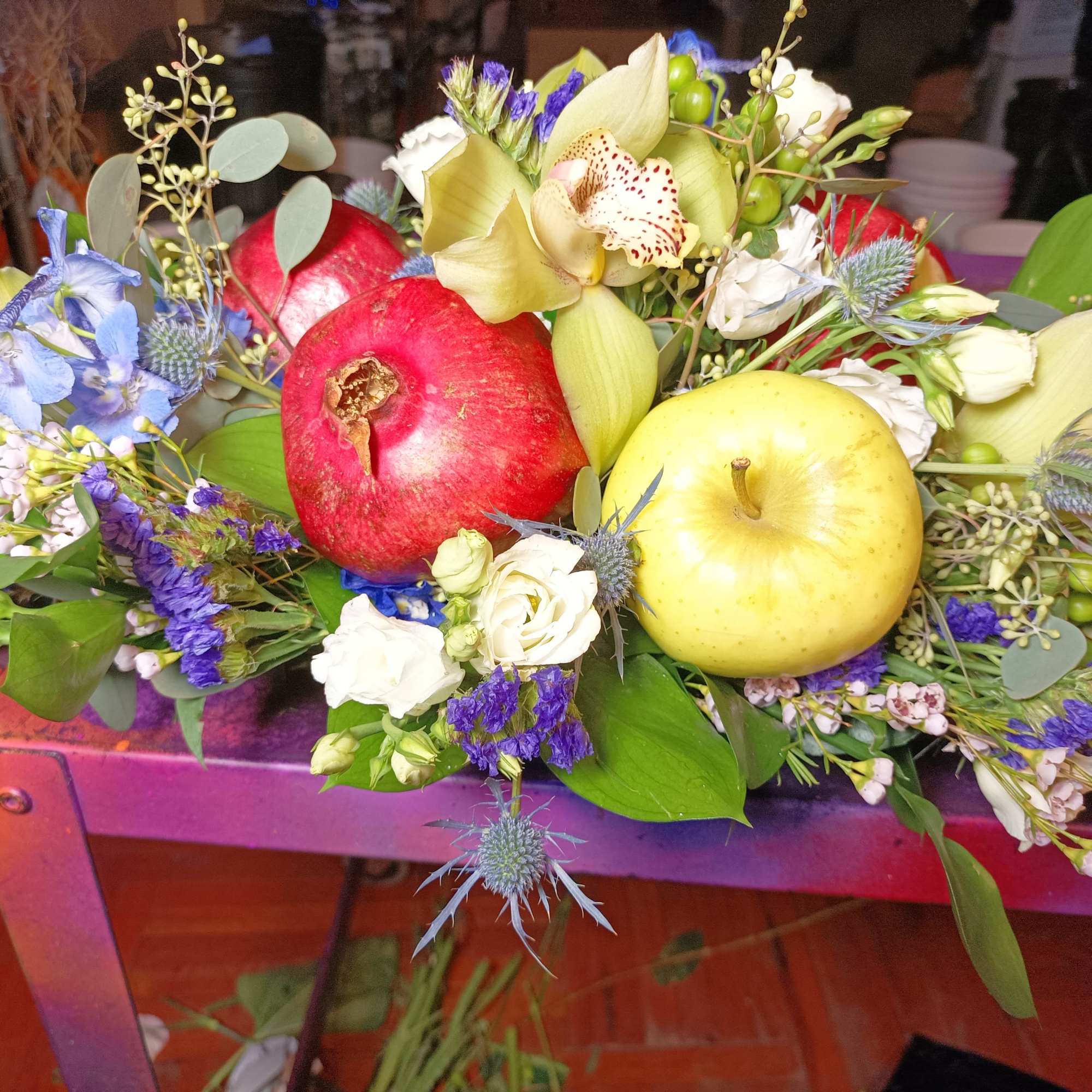 Mixed floral arrangement with pomegranates and apples on a purple table