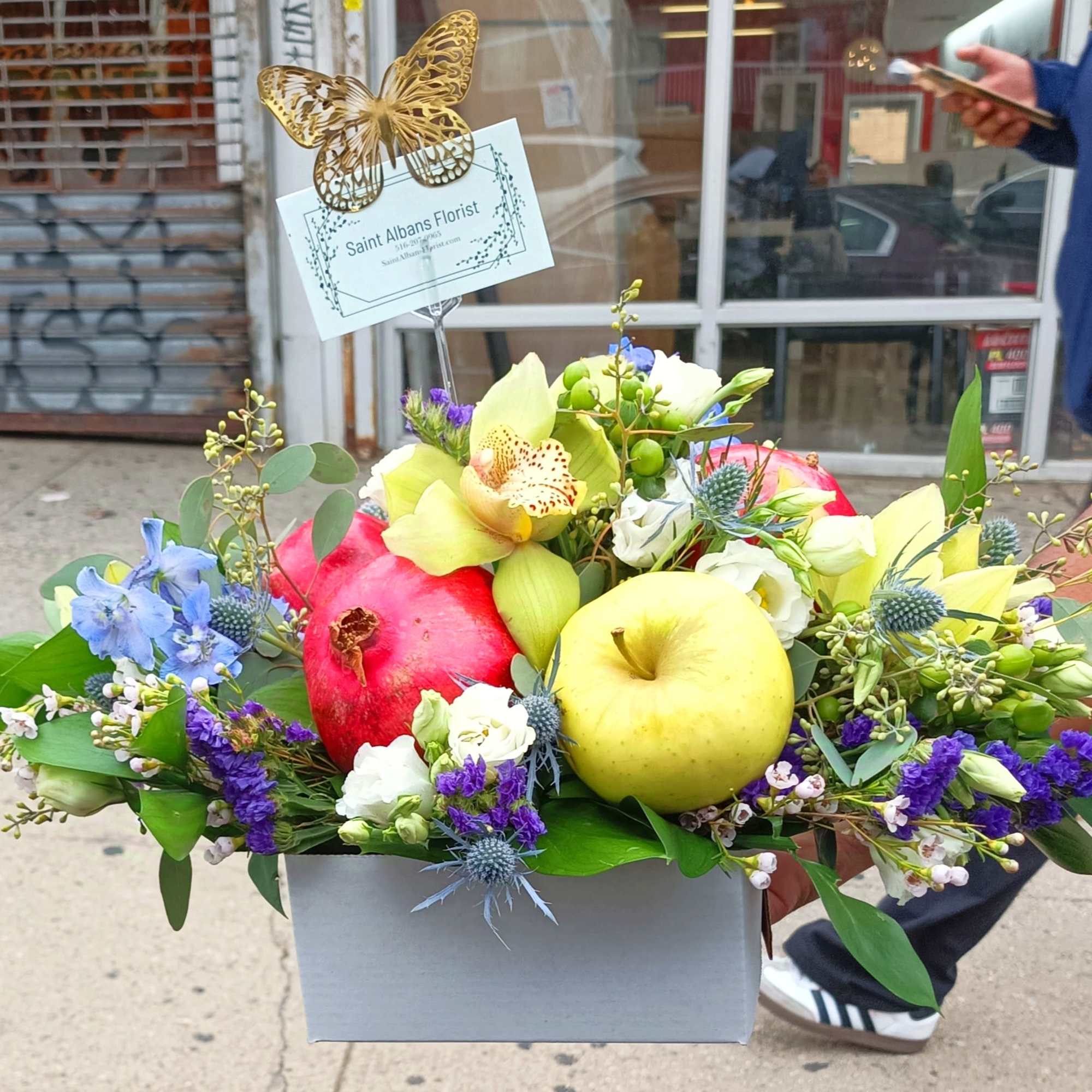 Colorful fruit and flower arrangement in a box with a butterfly card