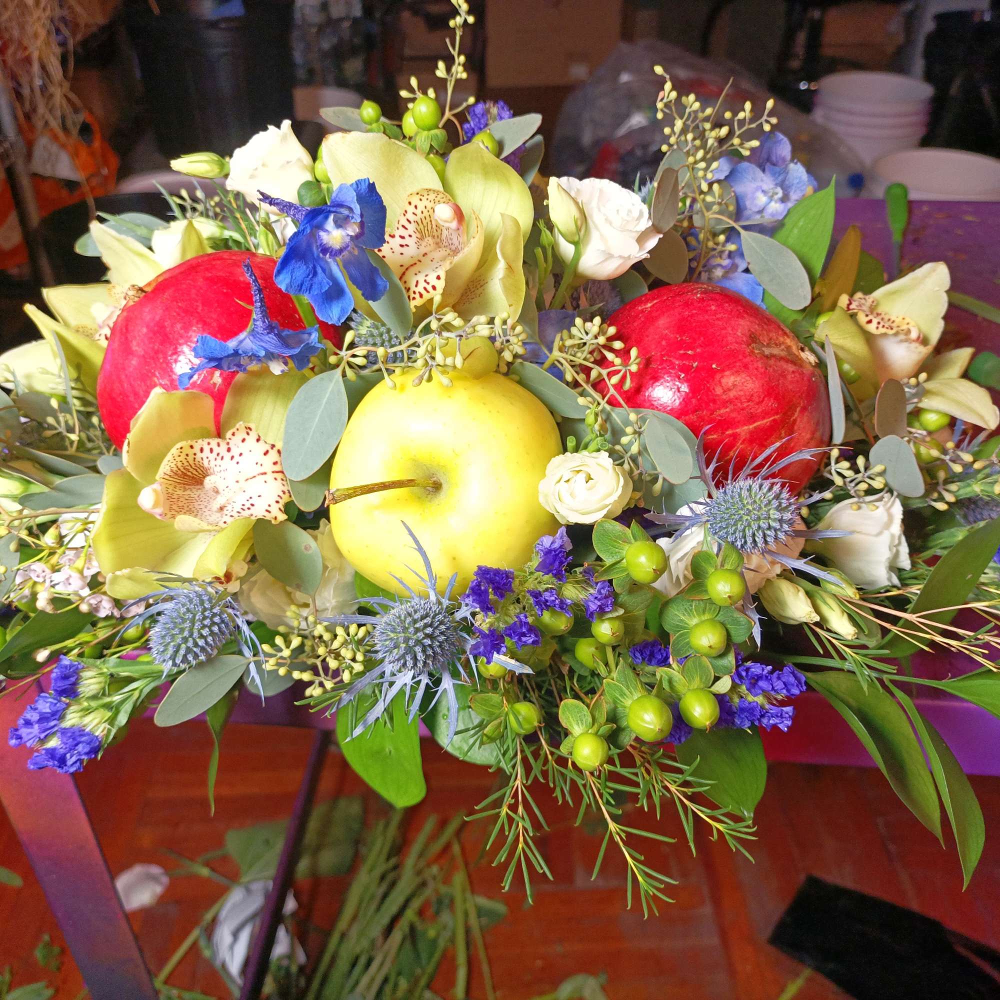 Fruit and flower centerpiece with apples, orchids, and blue thistles