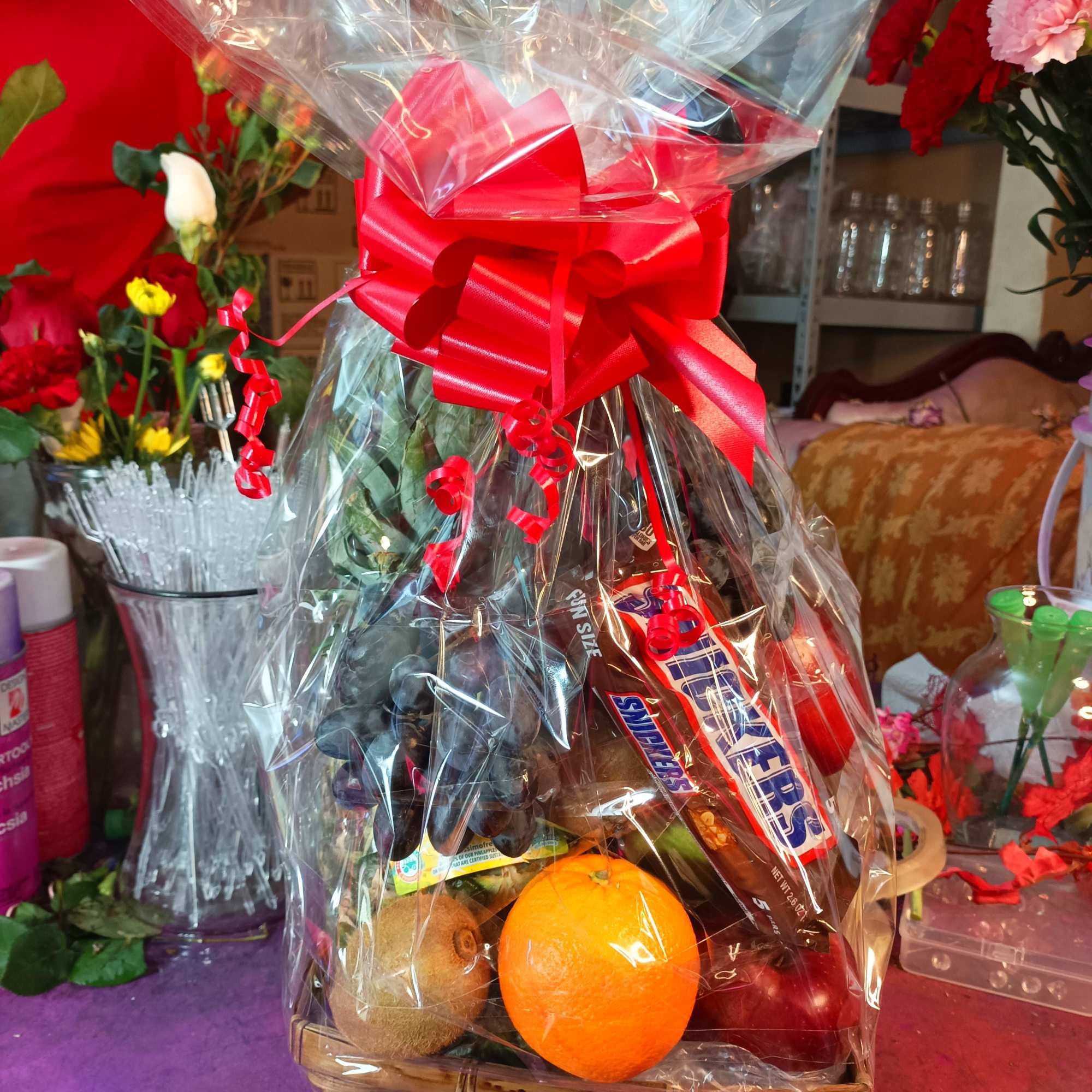 Gift basket with fruit and candy wrapped in clear cellophane and a red bow