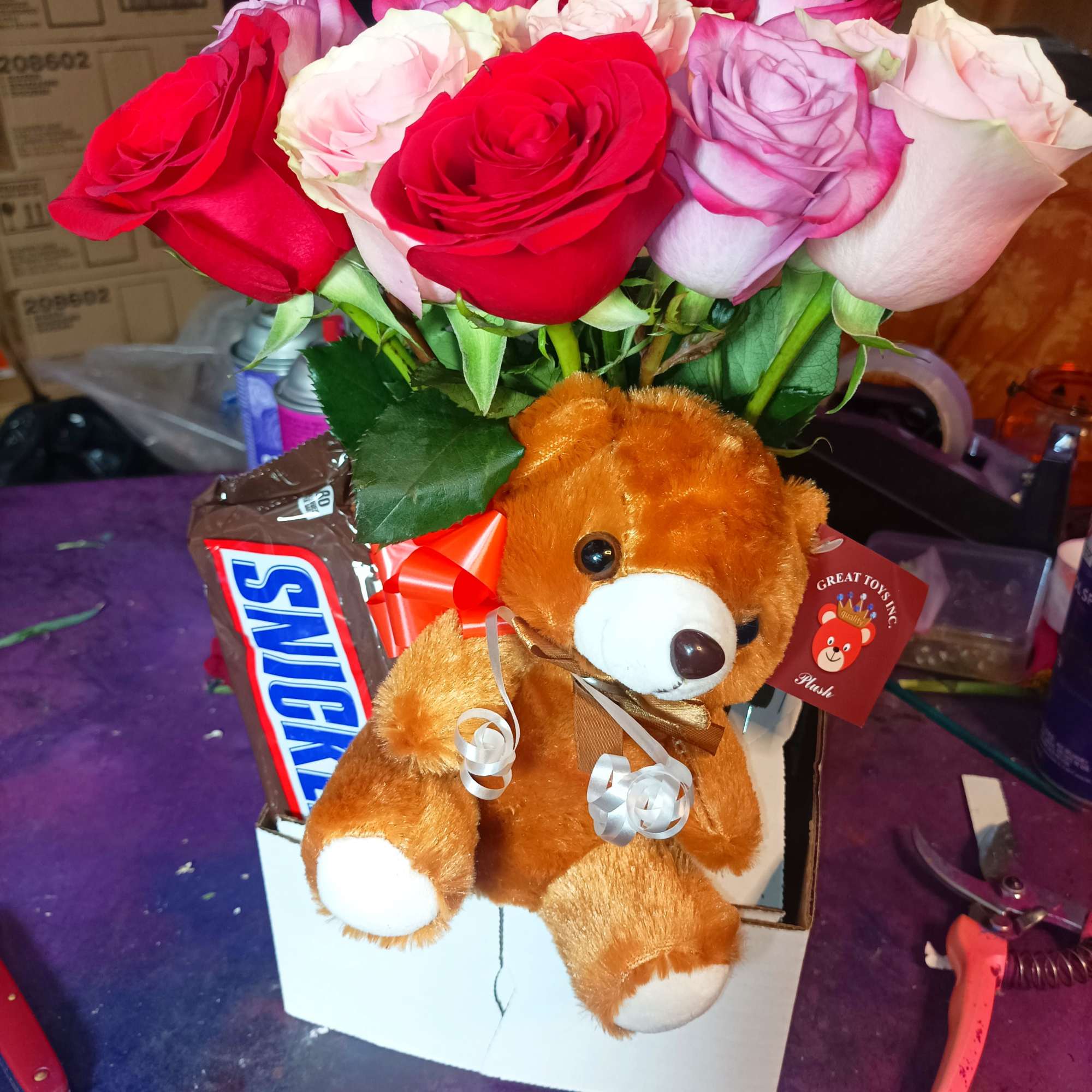 Bouquet of red, pink, and lavender roses with a teddy bear and candy box