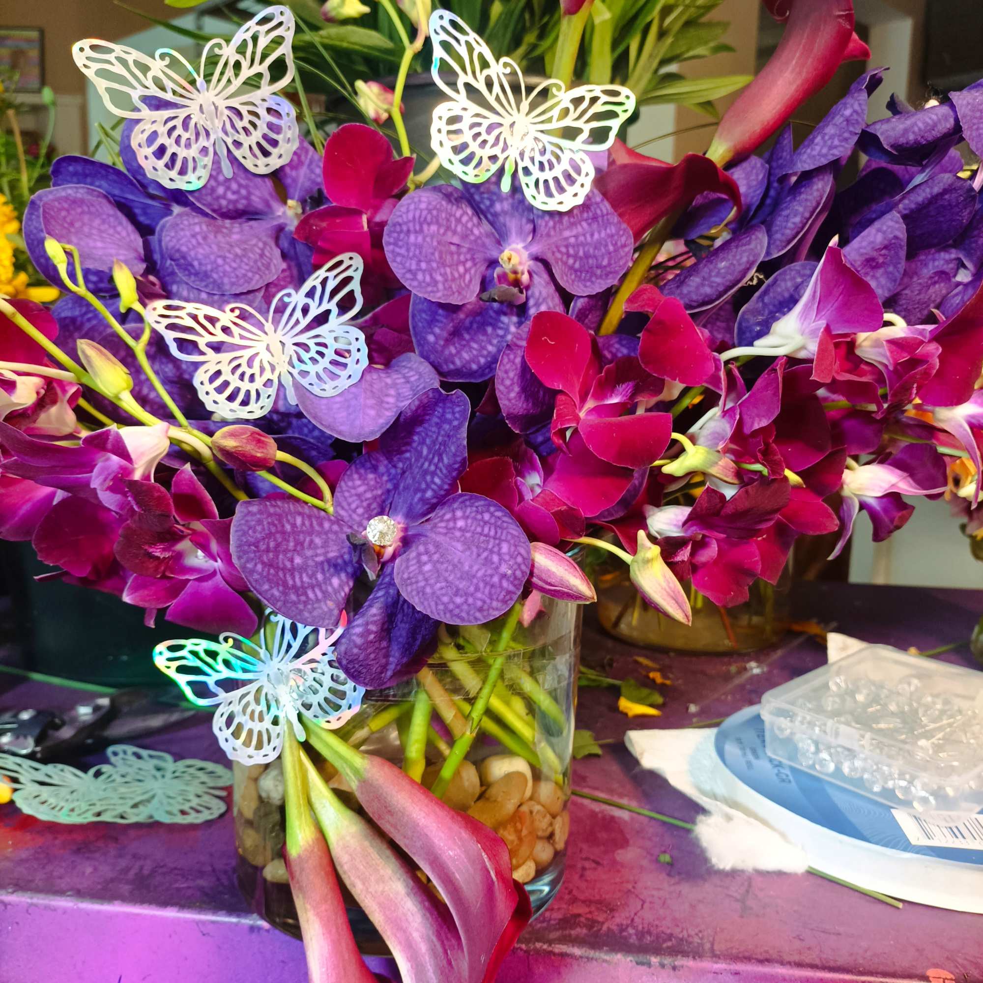 Purple orchids and pink calla lilies in a glass vase with butterfly picks