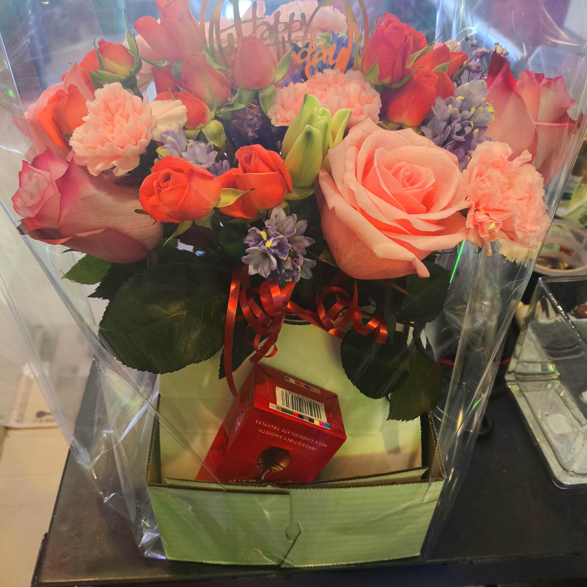 Mixed bouquet of pink roses, carnations, and purple flowers in a gift box