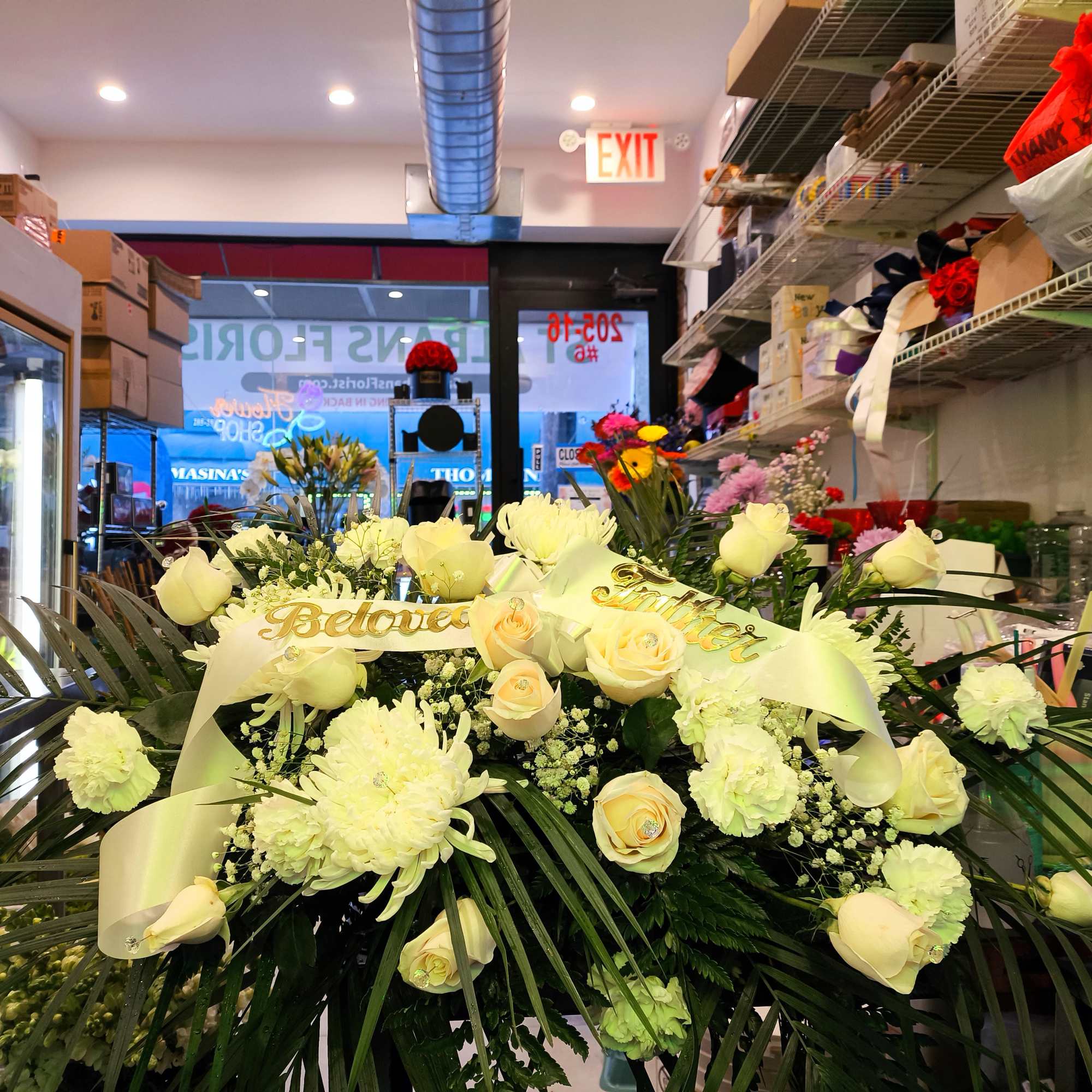 Large white floral arrangement with roses and ribbon in a shop