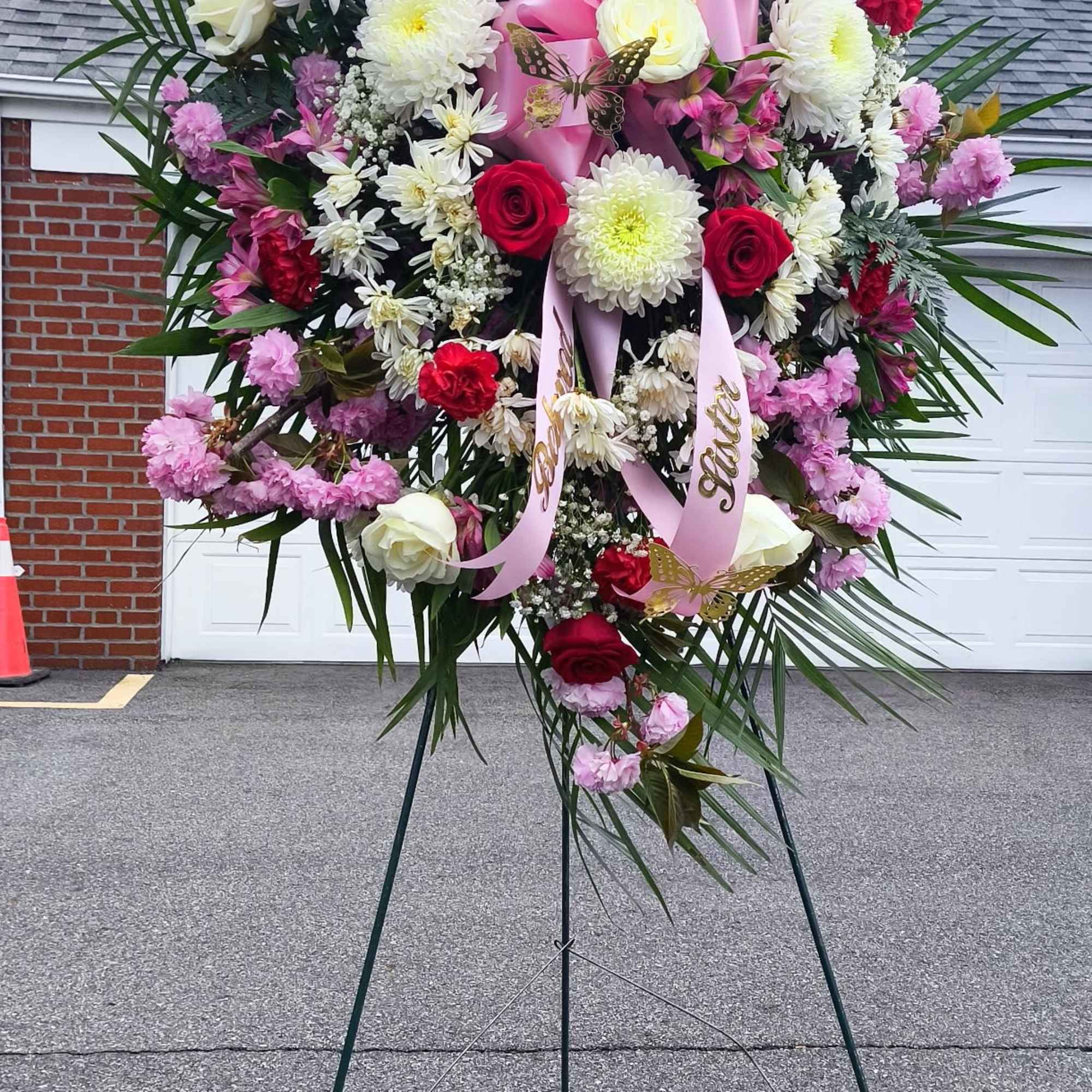 Large standing floral wreath with red, white, and pink flowers on an easel