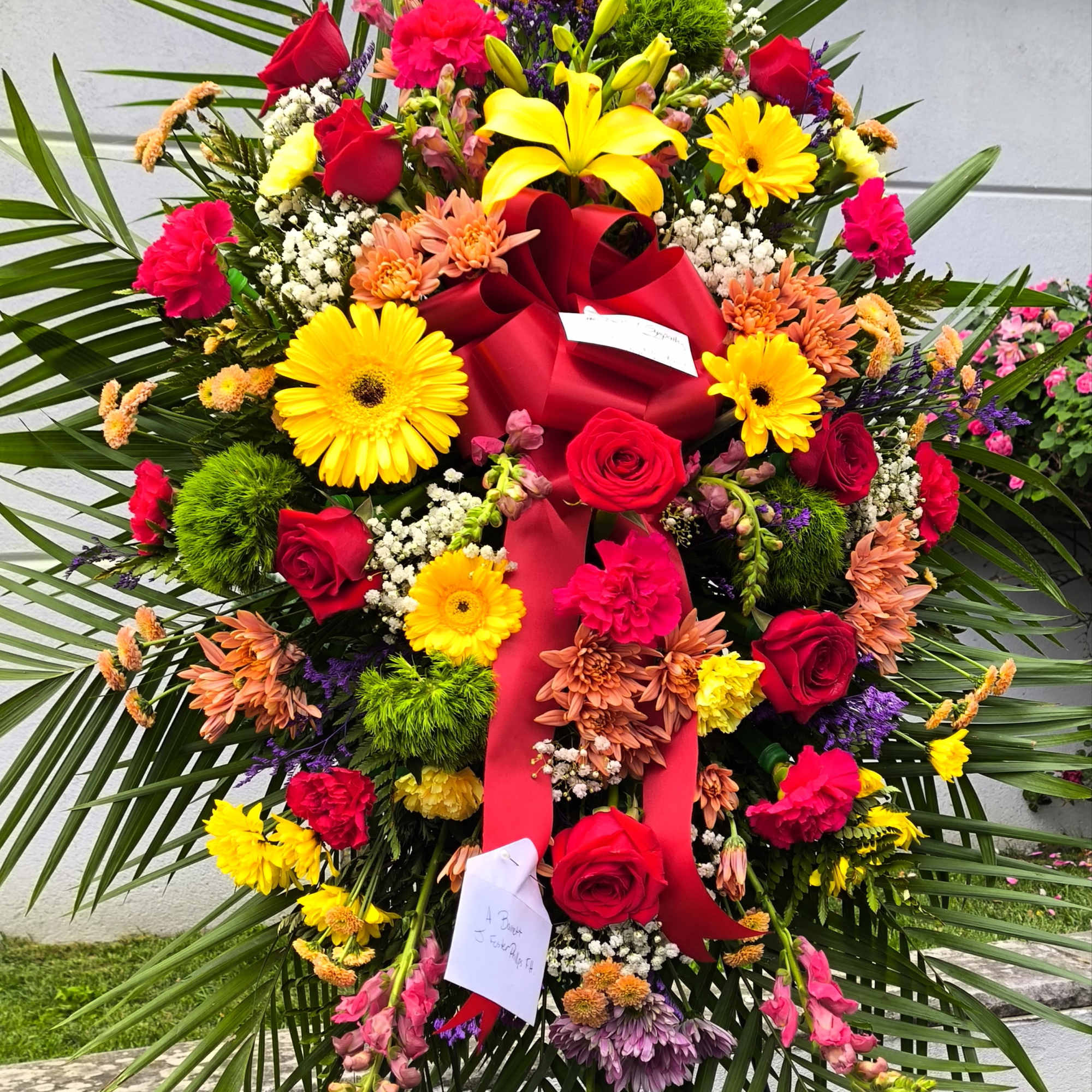 Large standing floral spray with red roses and yellow lilies on a red ribboned easel
