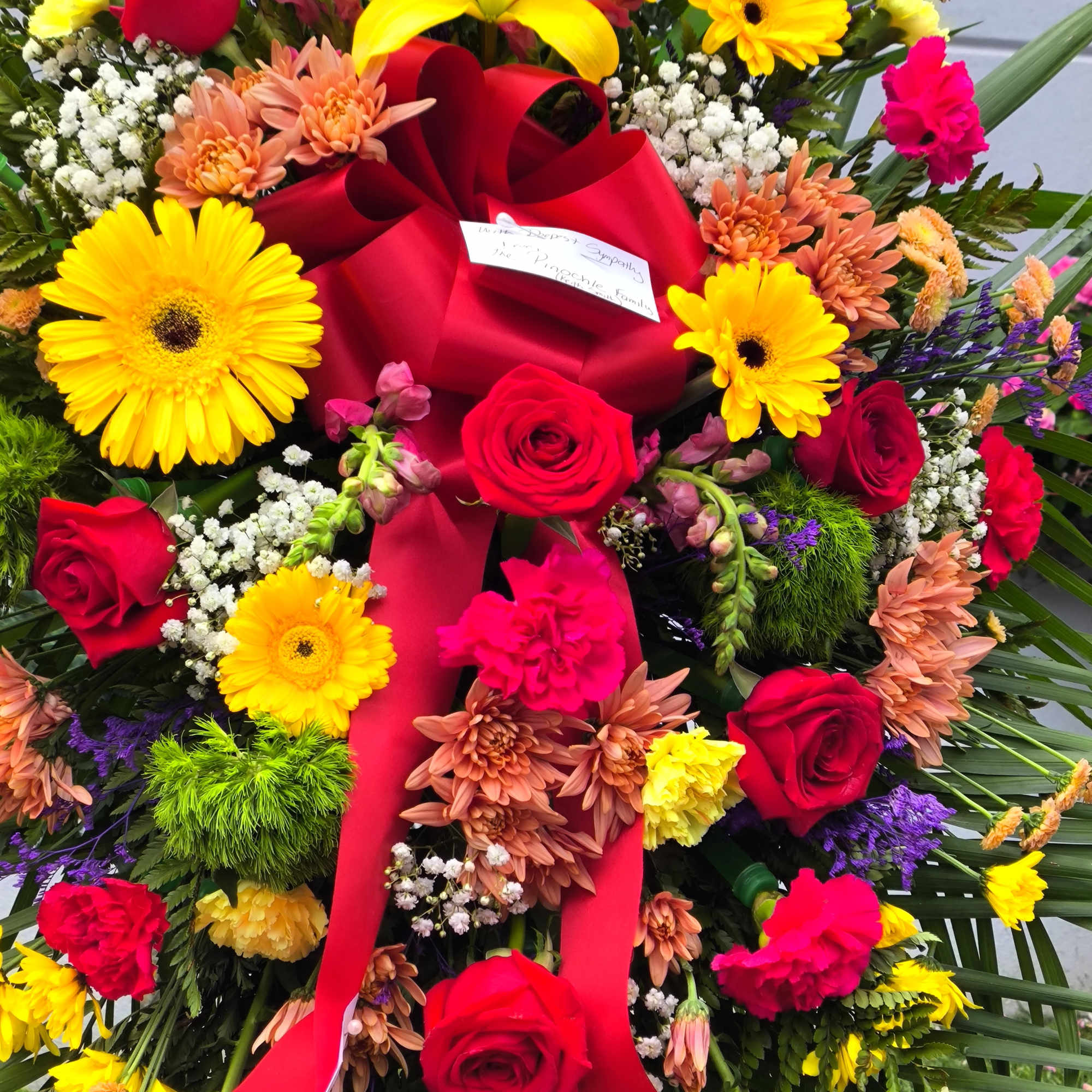 Large wreath of red roses, yellow daisies, and mixed flowers with a red ribbon