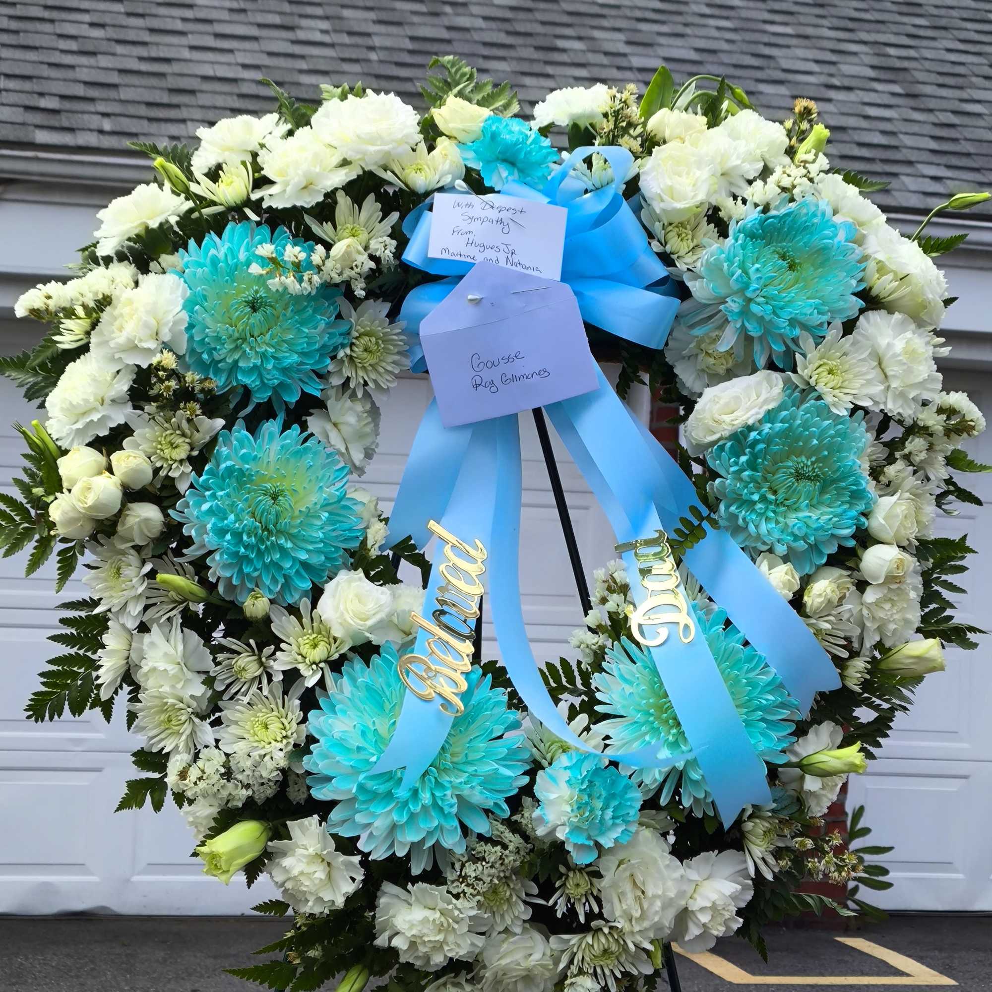 Large funeral wreath of white and turquoise flowers with blue ribbons
