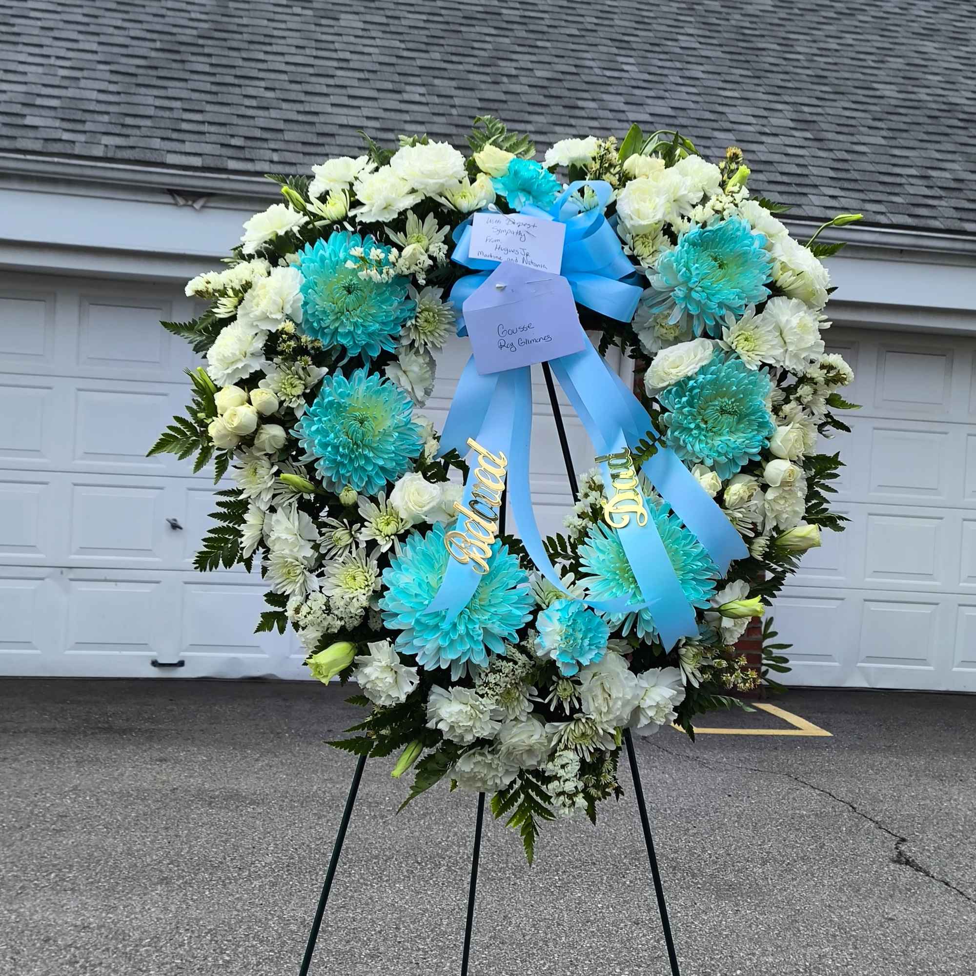 Large white and turquoise funeral wreath on an easel with blue ribbons