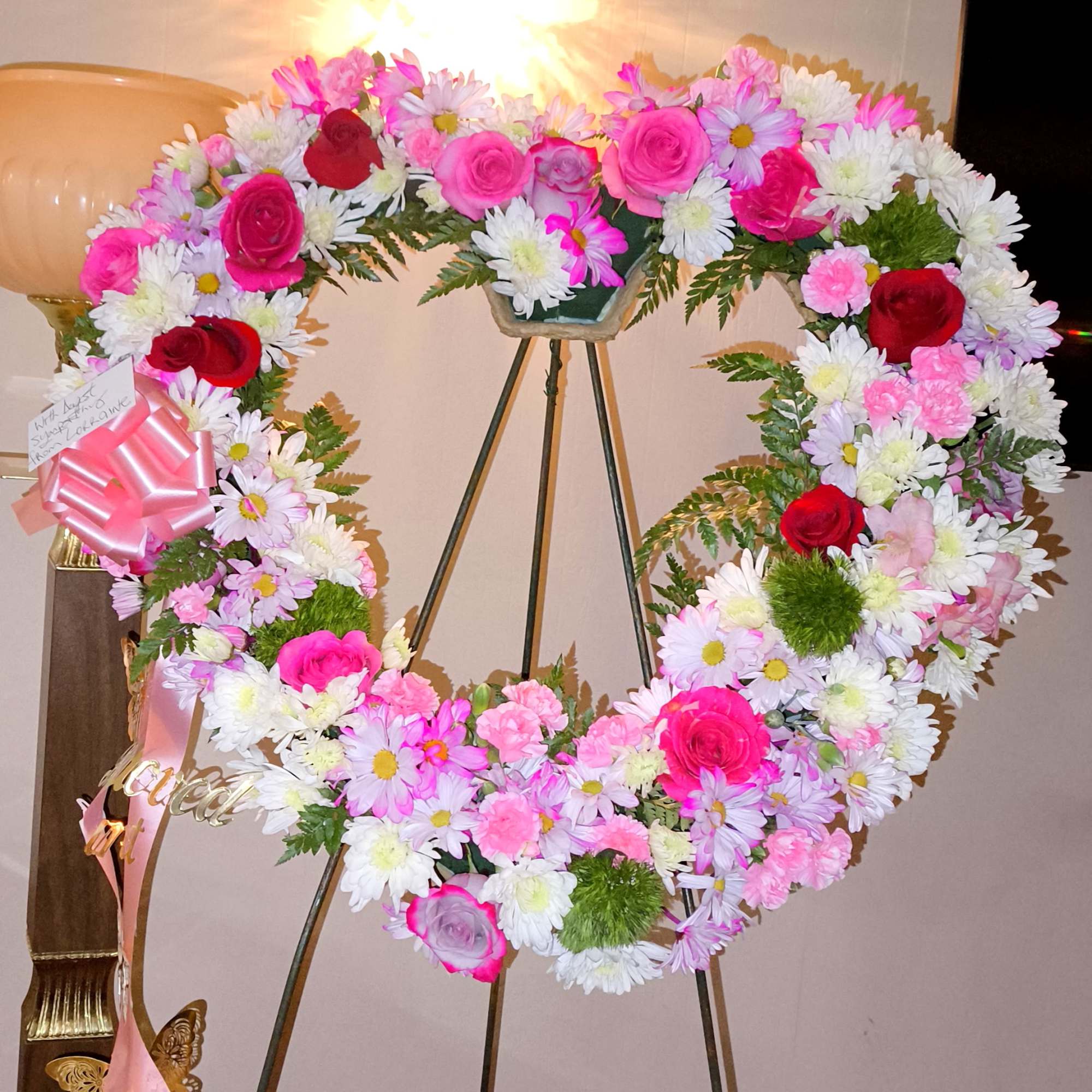 Heart-shaped floral wreath on a stand with pink and white flowers