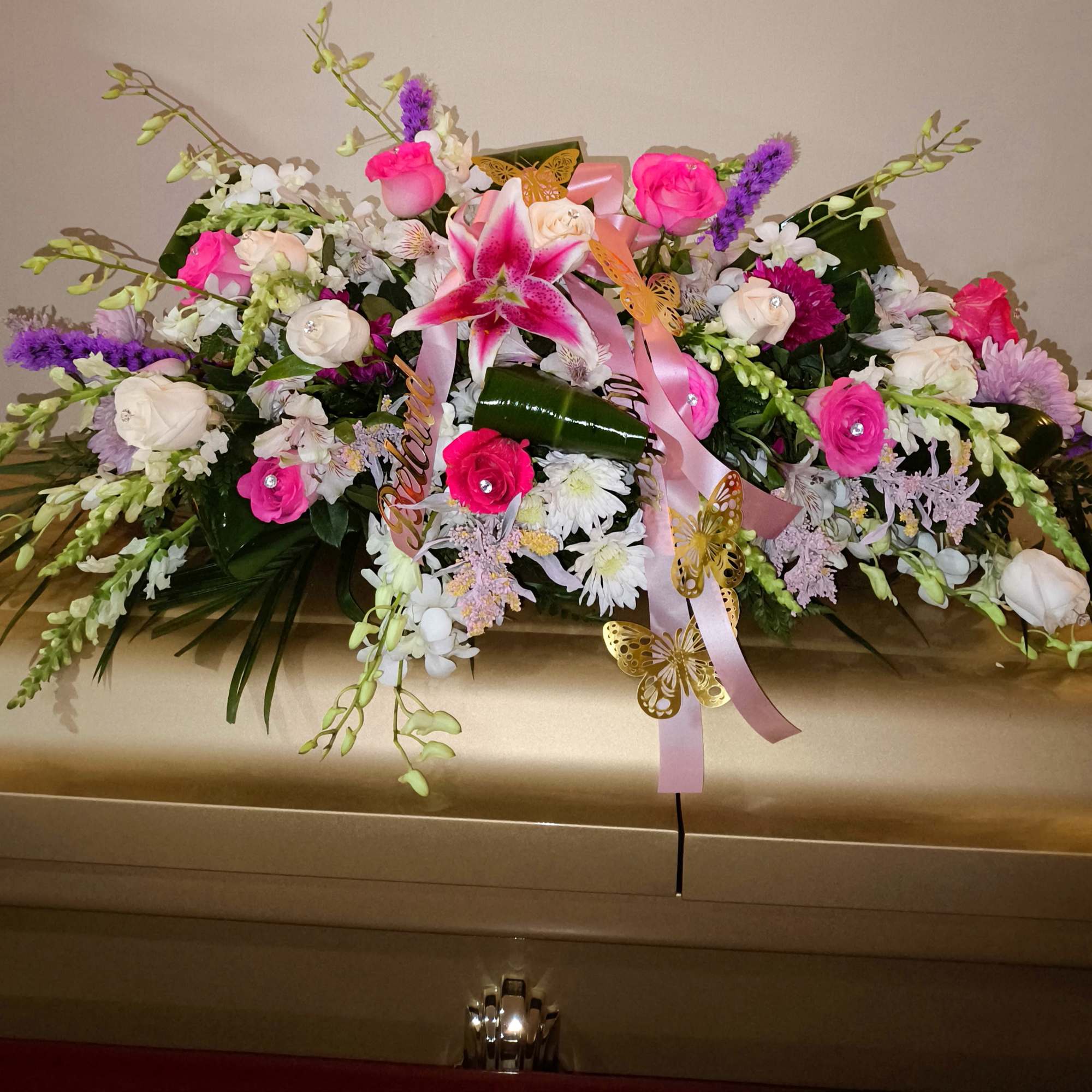 Pink and white floral casket spray with ribbons and butterfly accents