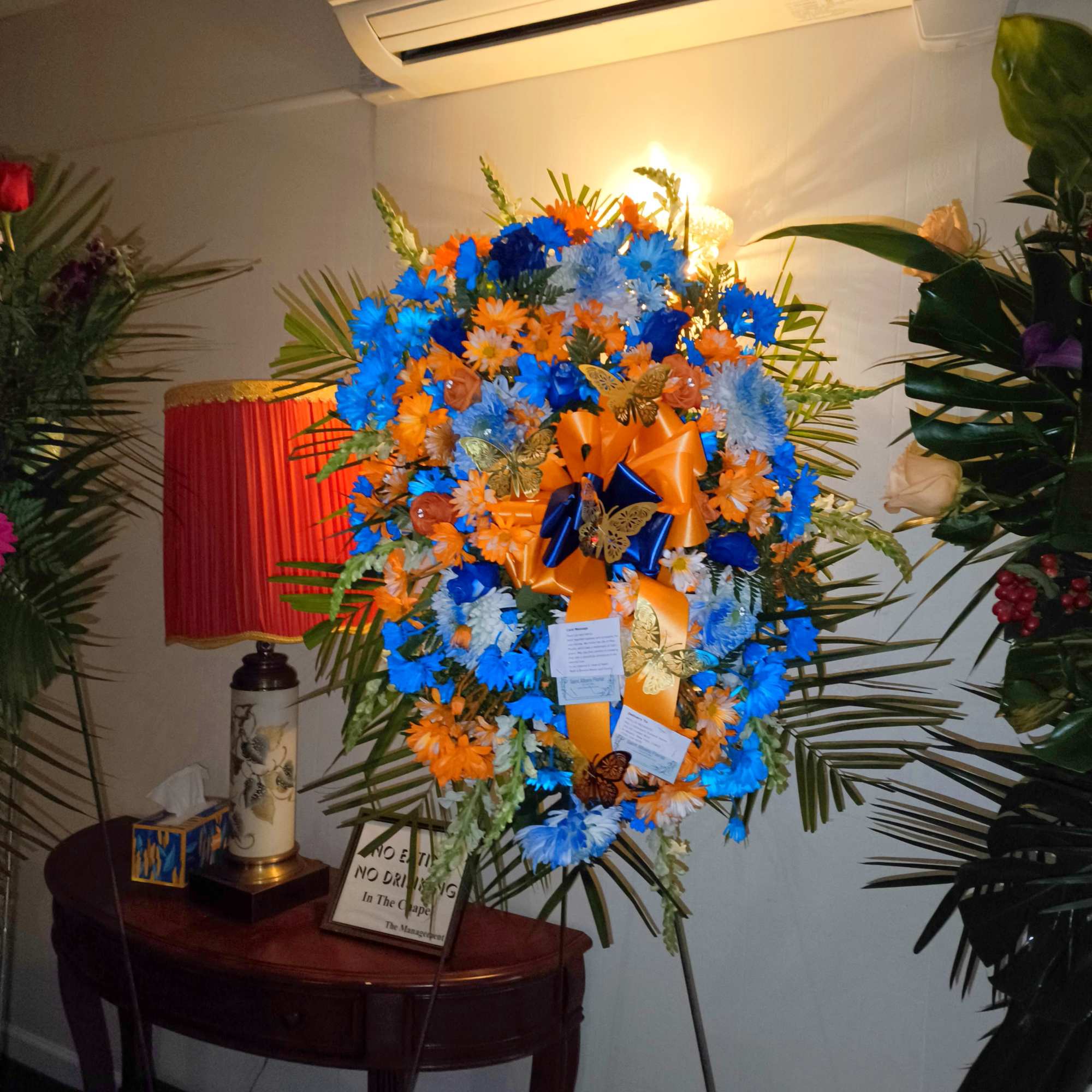 Large standing floral wreath with blue and orange flowers and ribbons