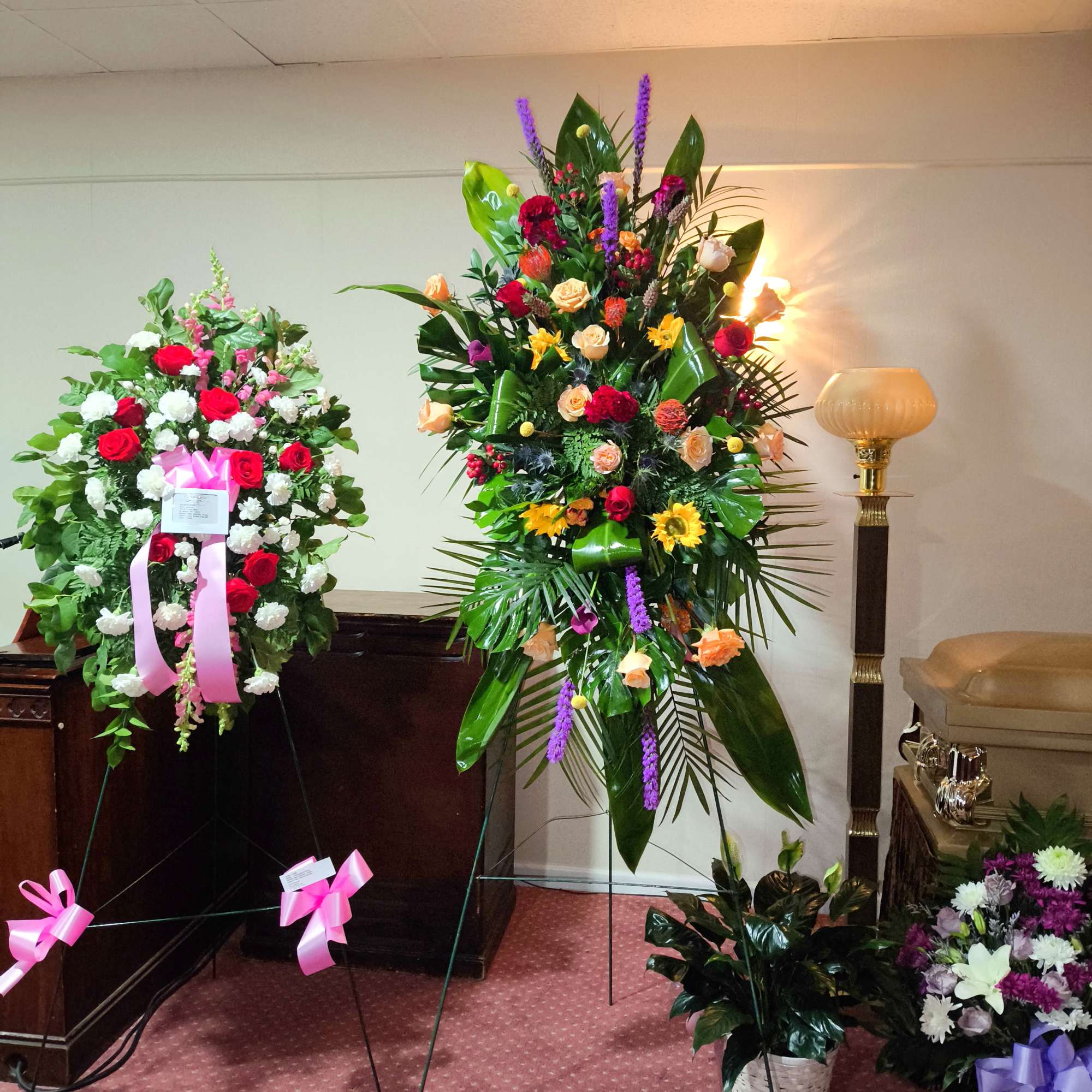 Two large floral standing sprays with ribbons in a room.