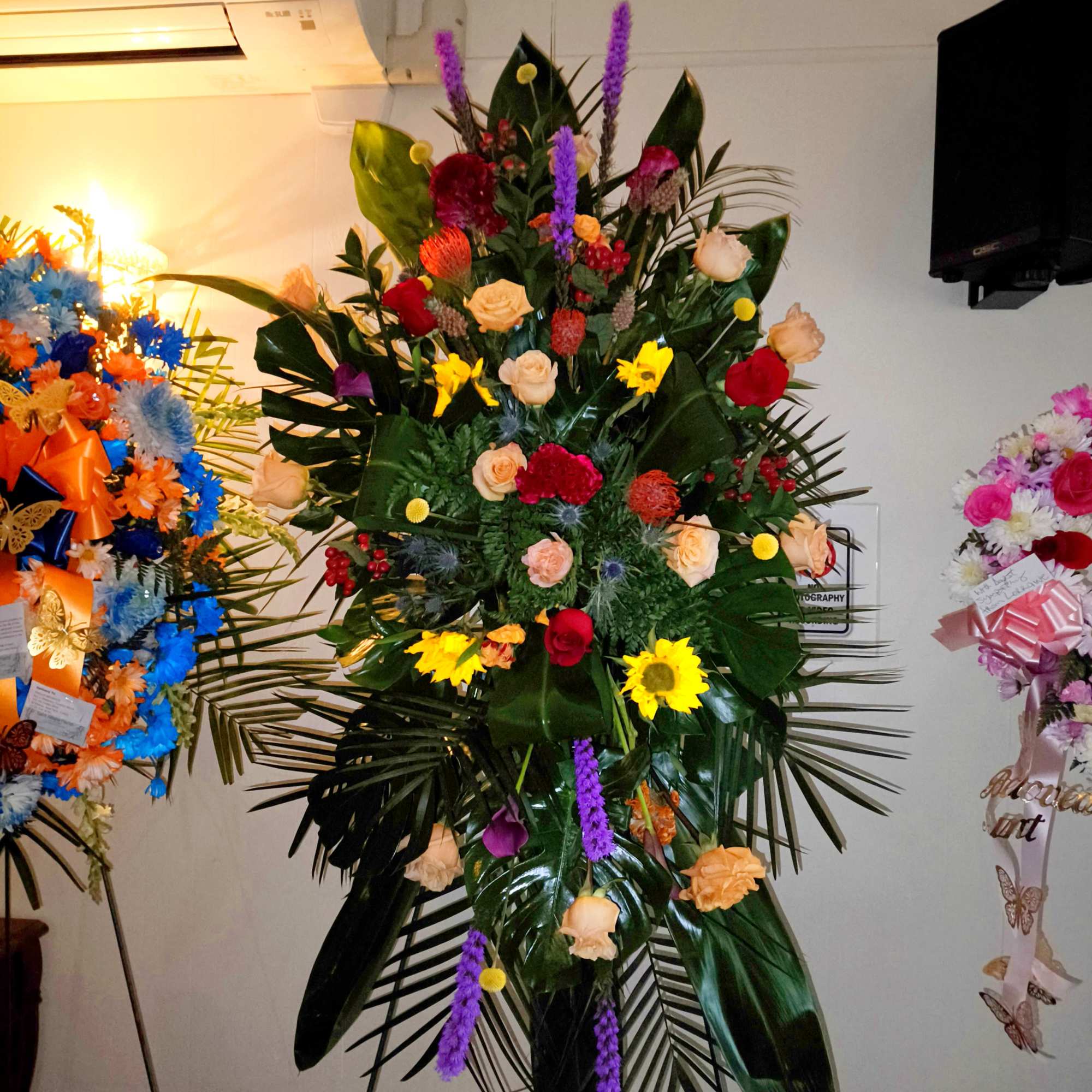 Tall floral standing spray with roses, sunflowers, and purple spikes