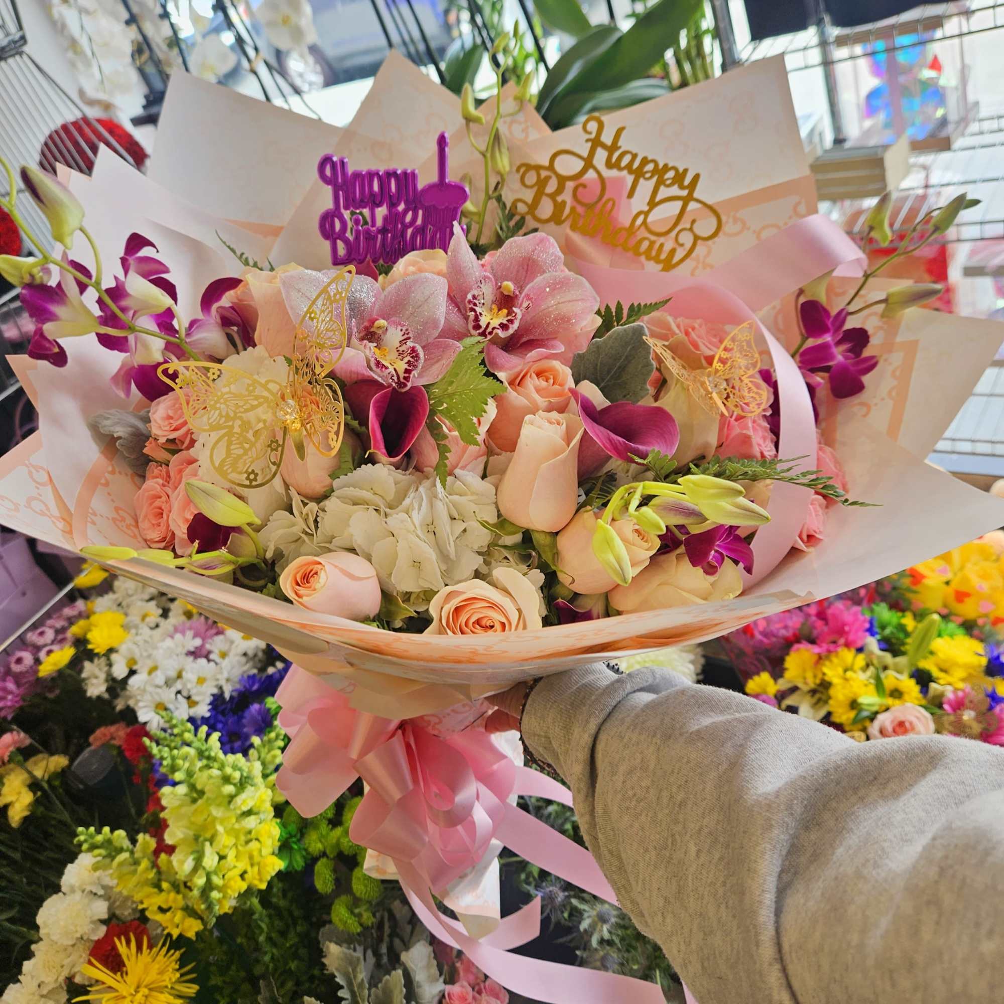 Pink and peach bouquet with orchids and roses, wrapped in pale paper