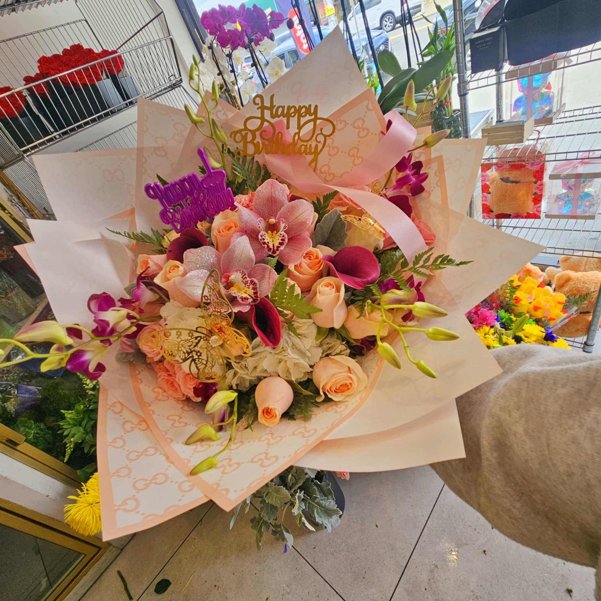 Large bouquet of pink and peach flowers with a birthday topper and ribbon