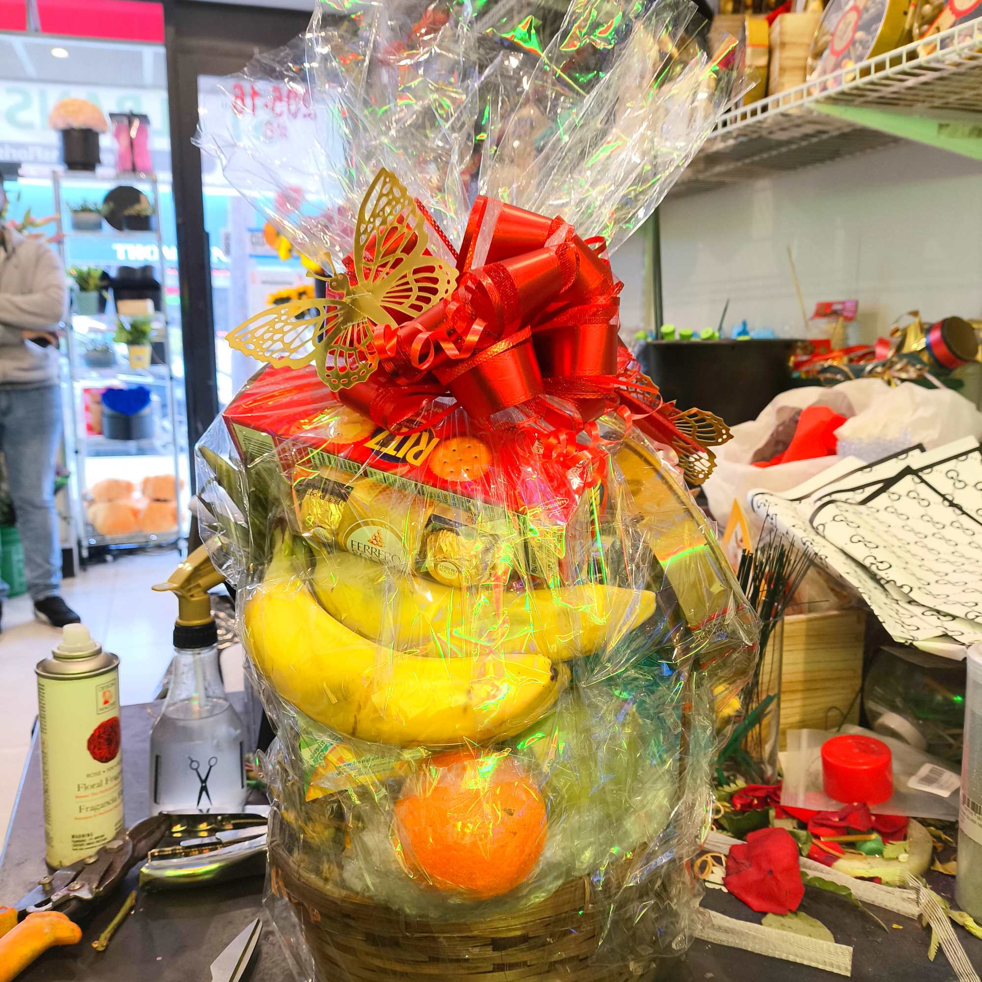 Gift basket with bananas, oranges, and chocolates wrapped in clear cellophane