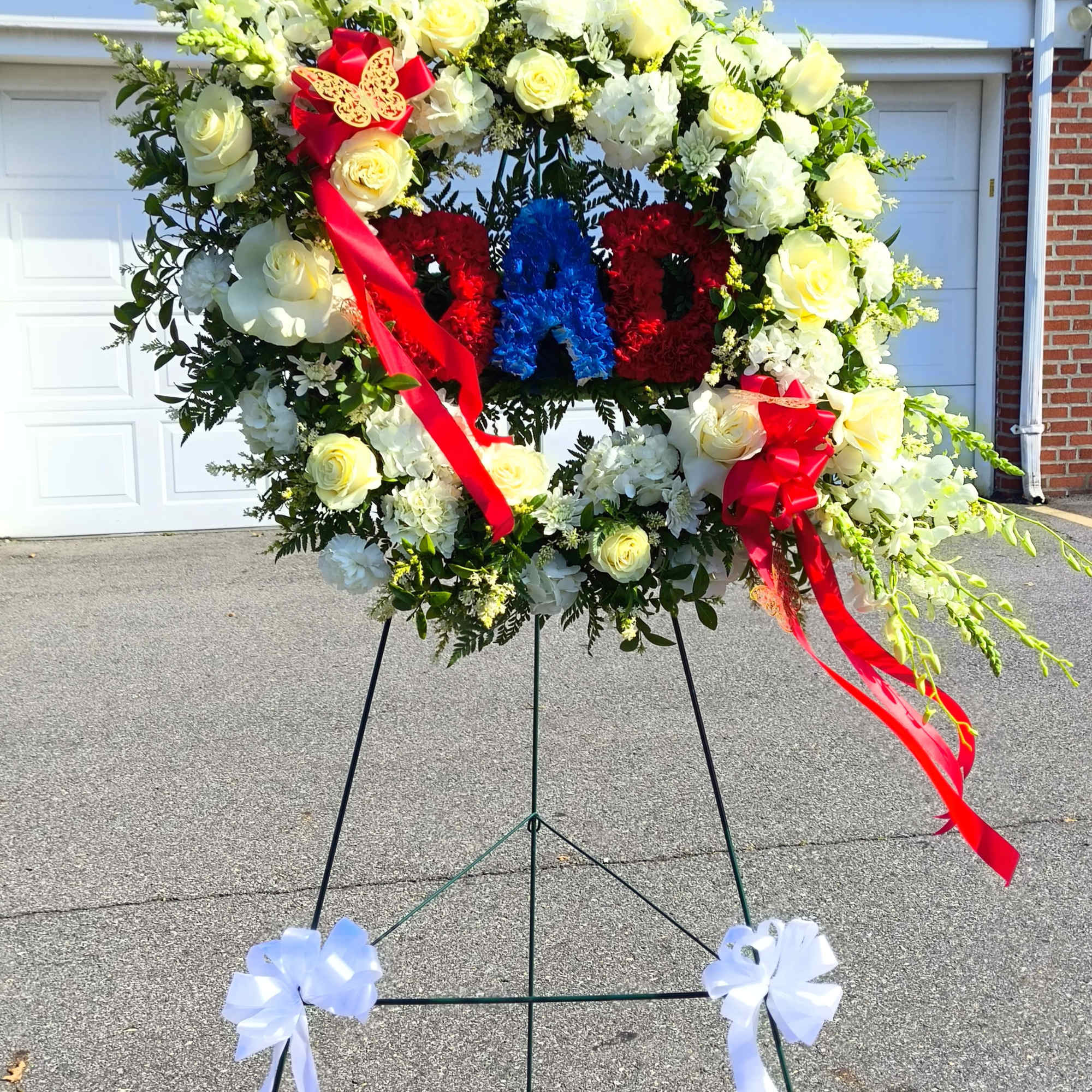 Large floral wreath on an easel with red and blue ribbon accents
