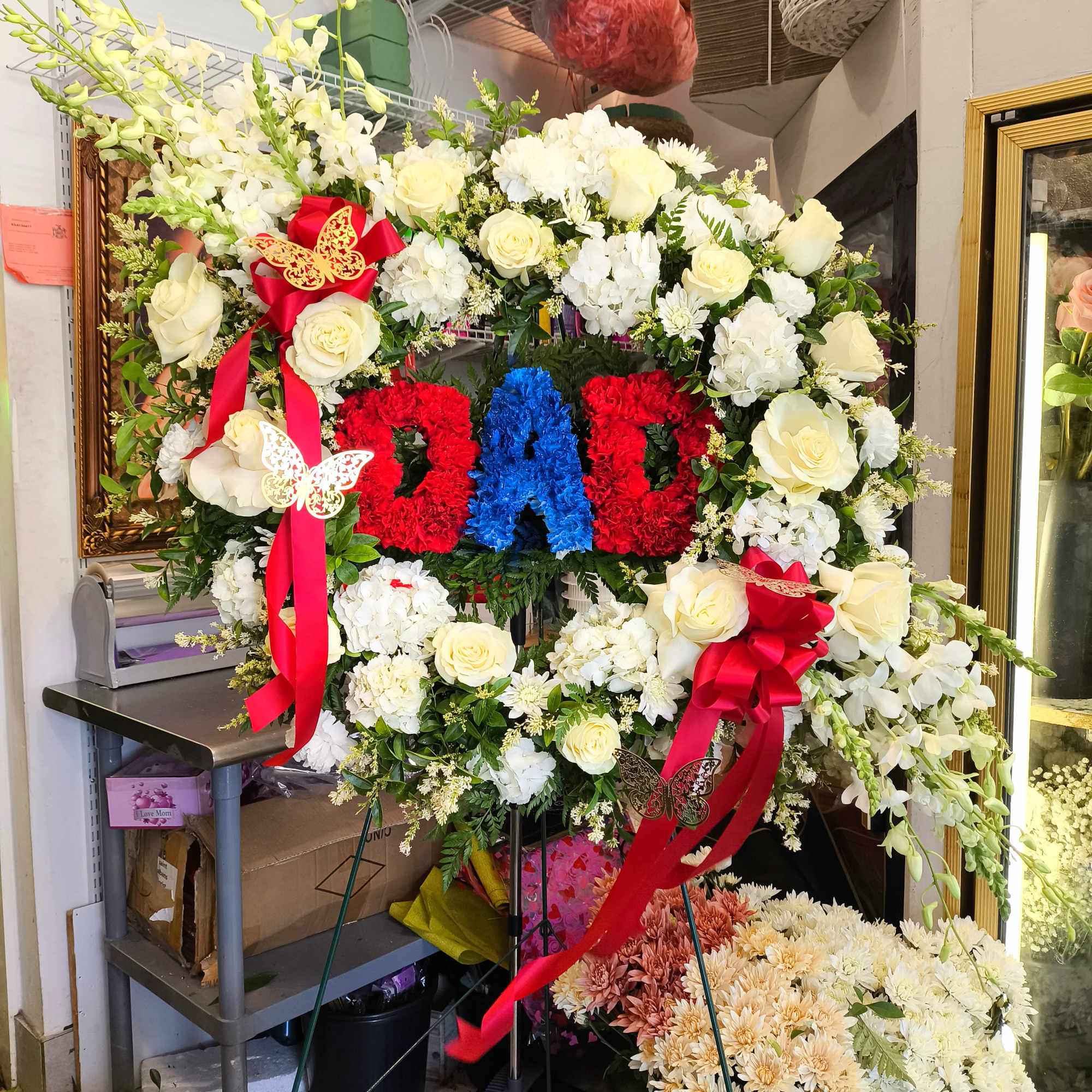 Large standing floral wreath with white roses and red ribbon bows