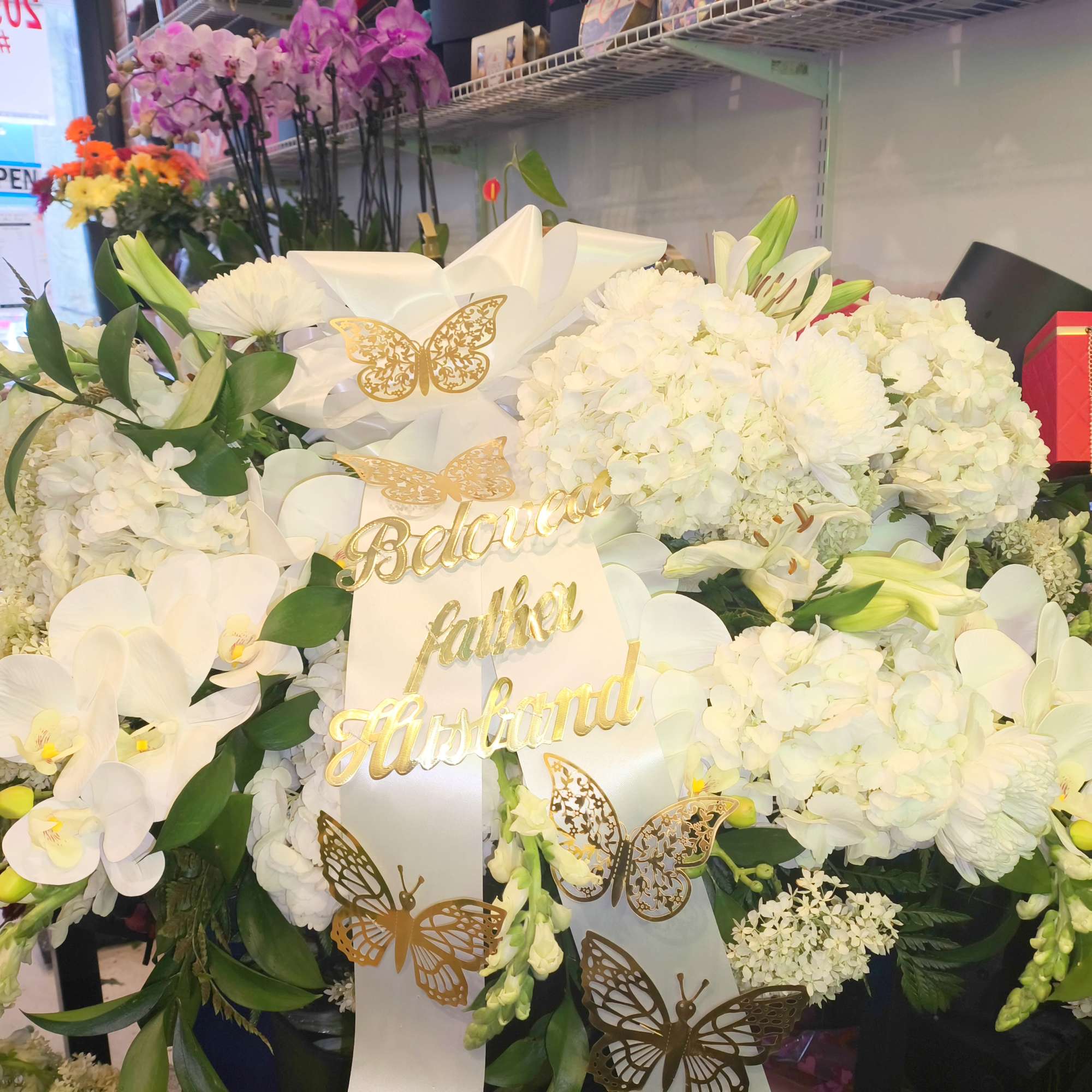 Large white floral arrangement with orchids and hydrangeas, decorated with gold butterflies