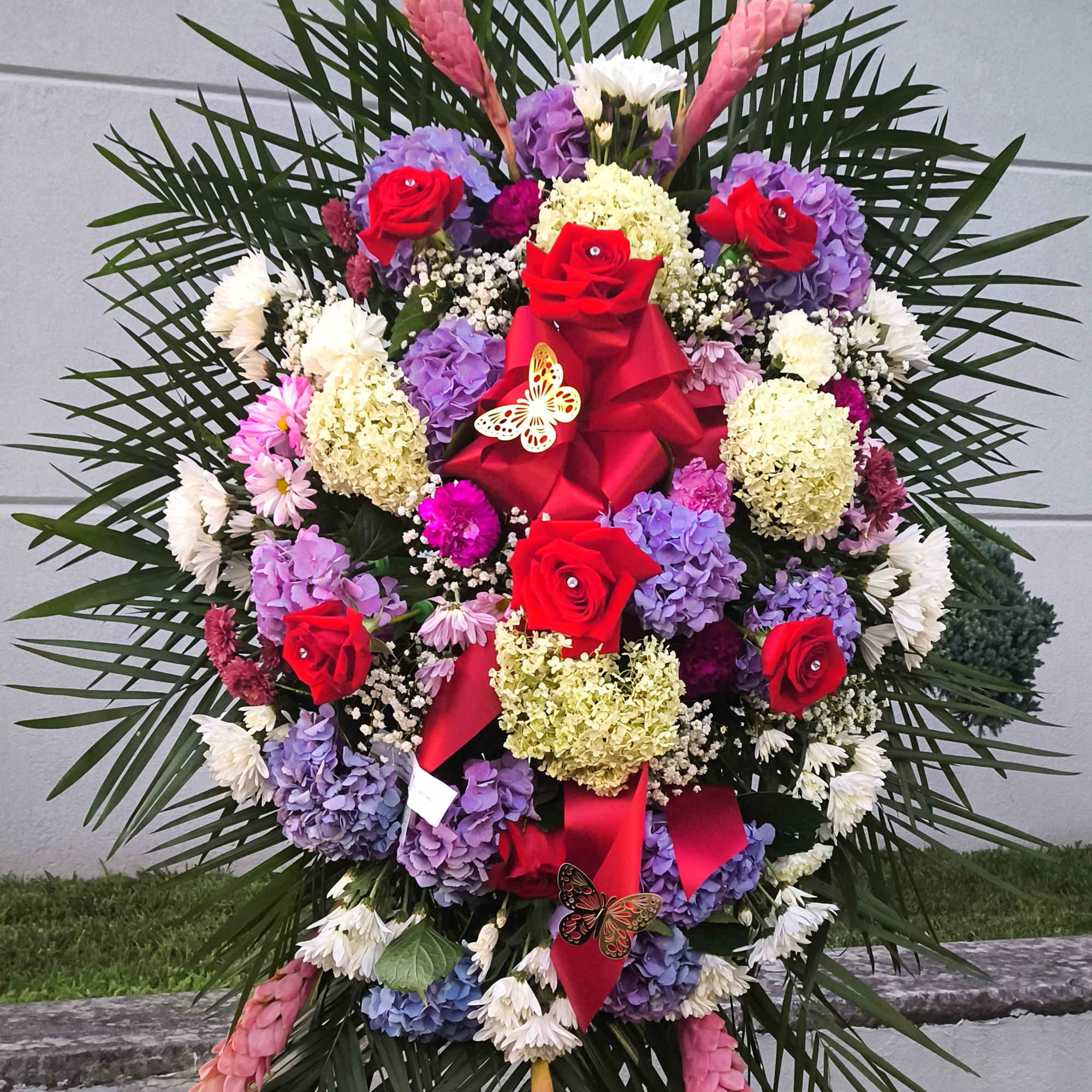 Large standing floral spray with red roses, hydrangeas, and palm fronds