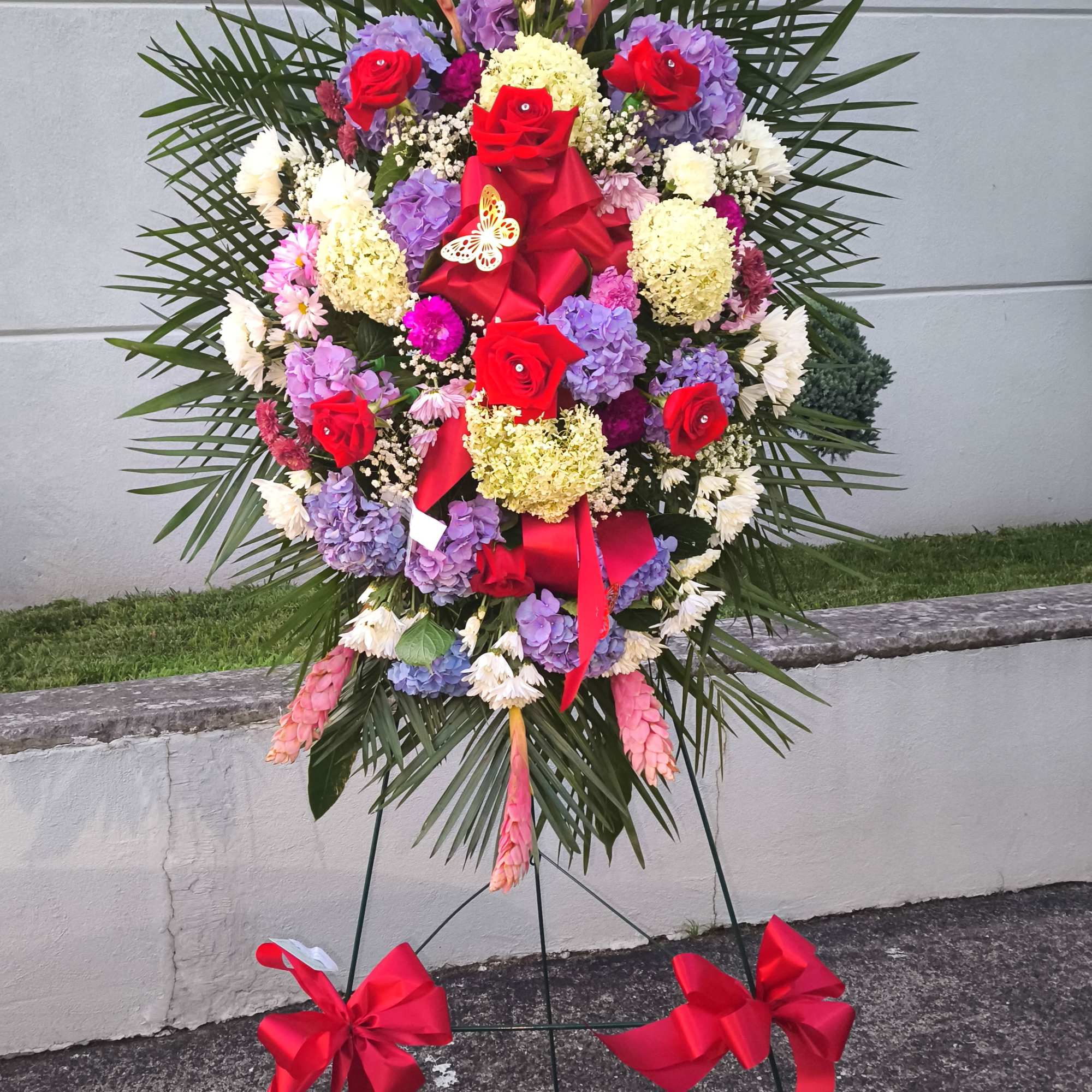 Standing floral wreath with red roses and purple hydrangeas on an easel