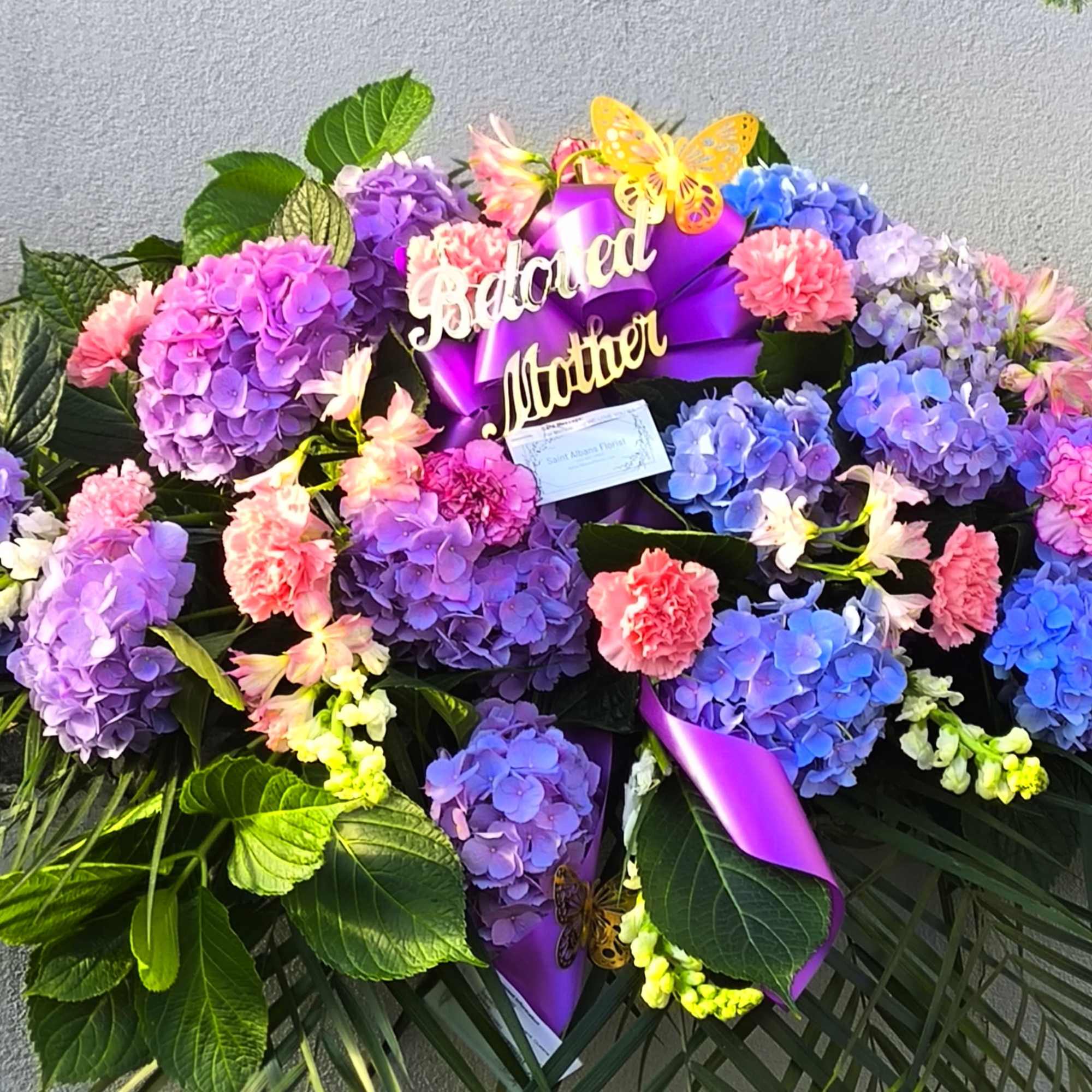 Large floral arrangement with purple hydrangeas, pink carnations, and a purple ribbon
